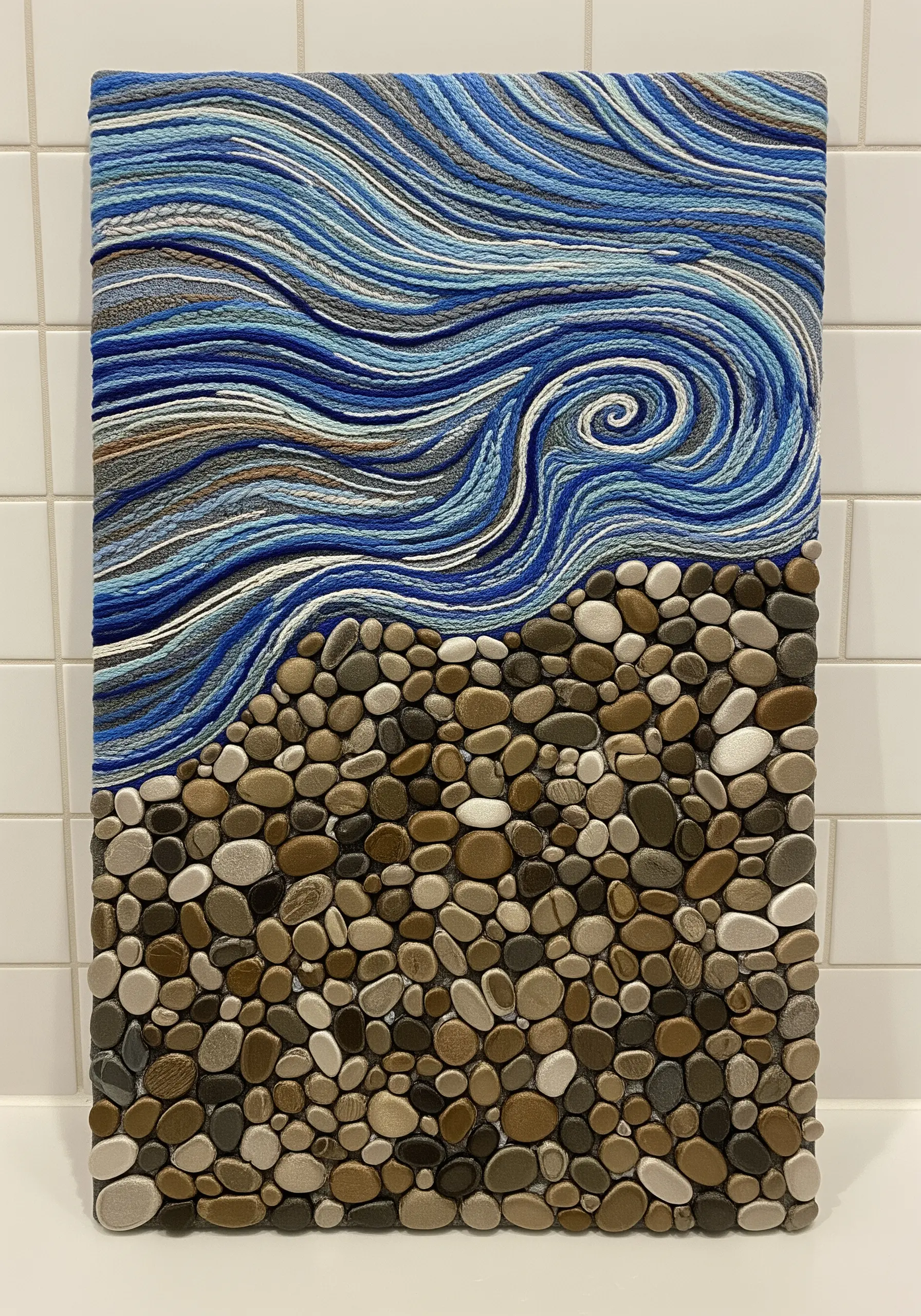 A mixed-media artwork showing swirling blue yarn for waves and small sculpted stones for a beach.