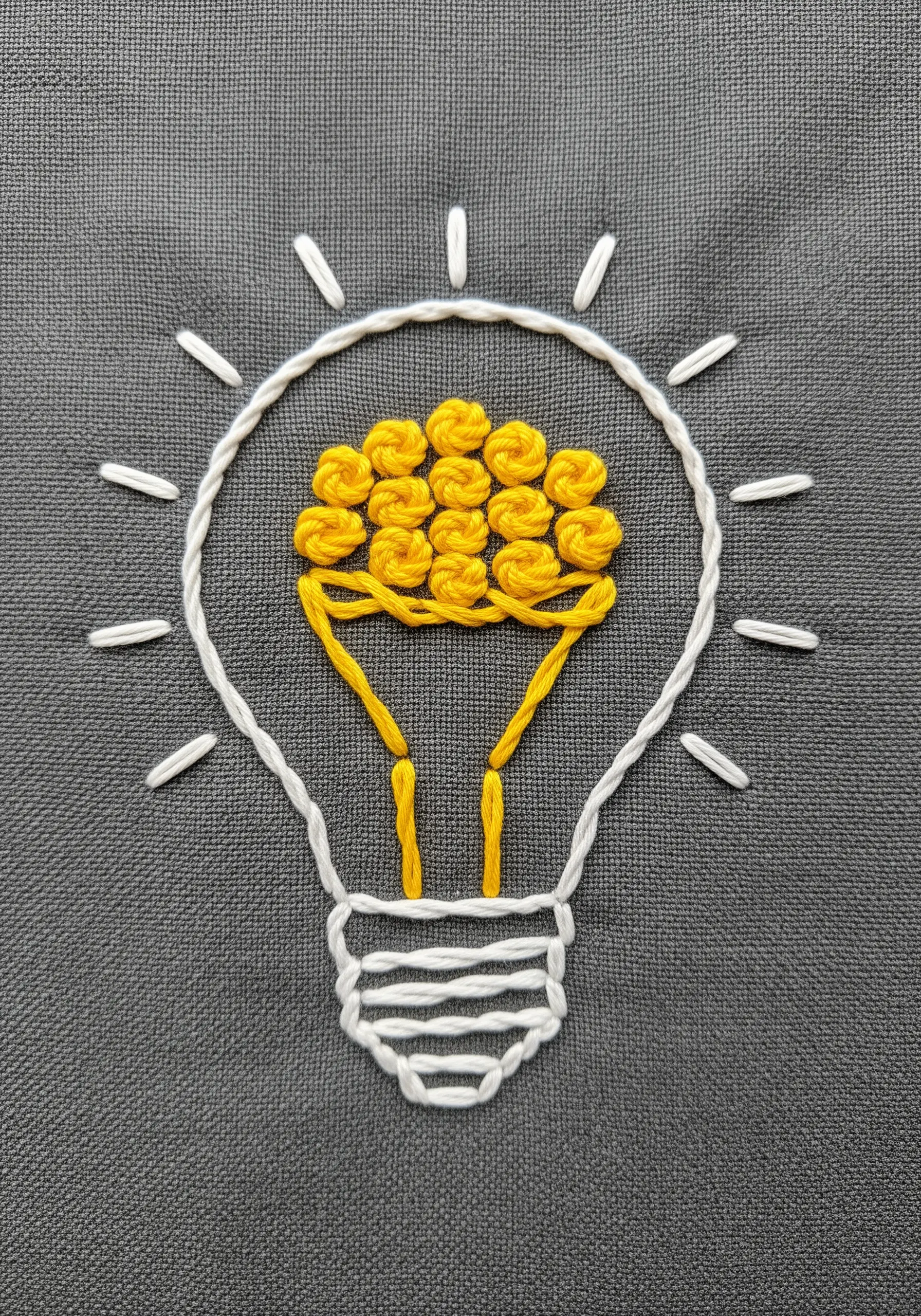 An embroidered lightbulb with a filament made of yellow woven wheel stitches.