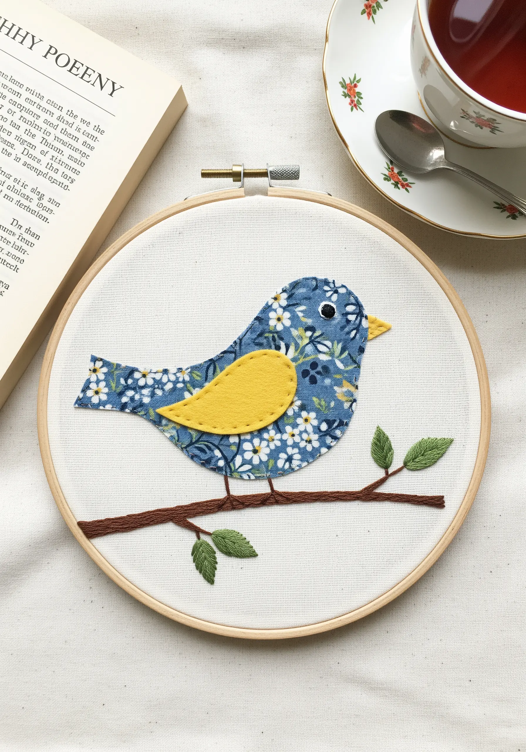 A bird made from blue floral fabric with a solid yellow wing, sitting on an embroidered branch.