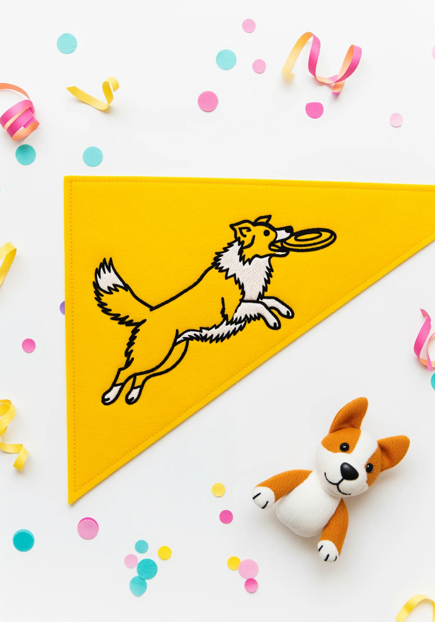 An embroidered dog catching a frisbee on a yellow felt pennant.