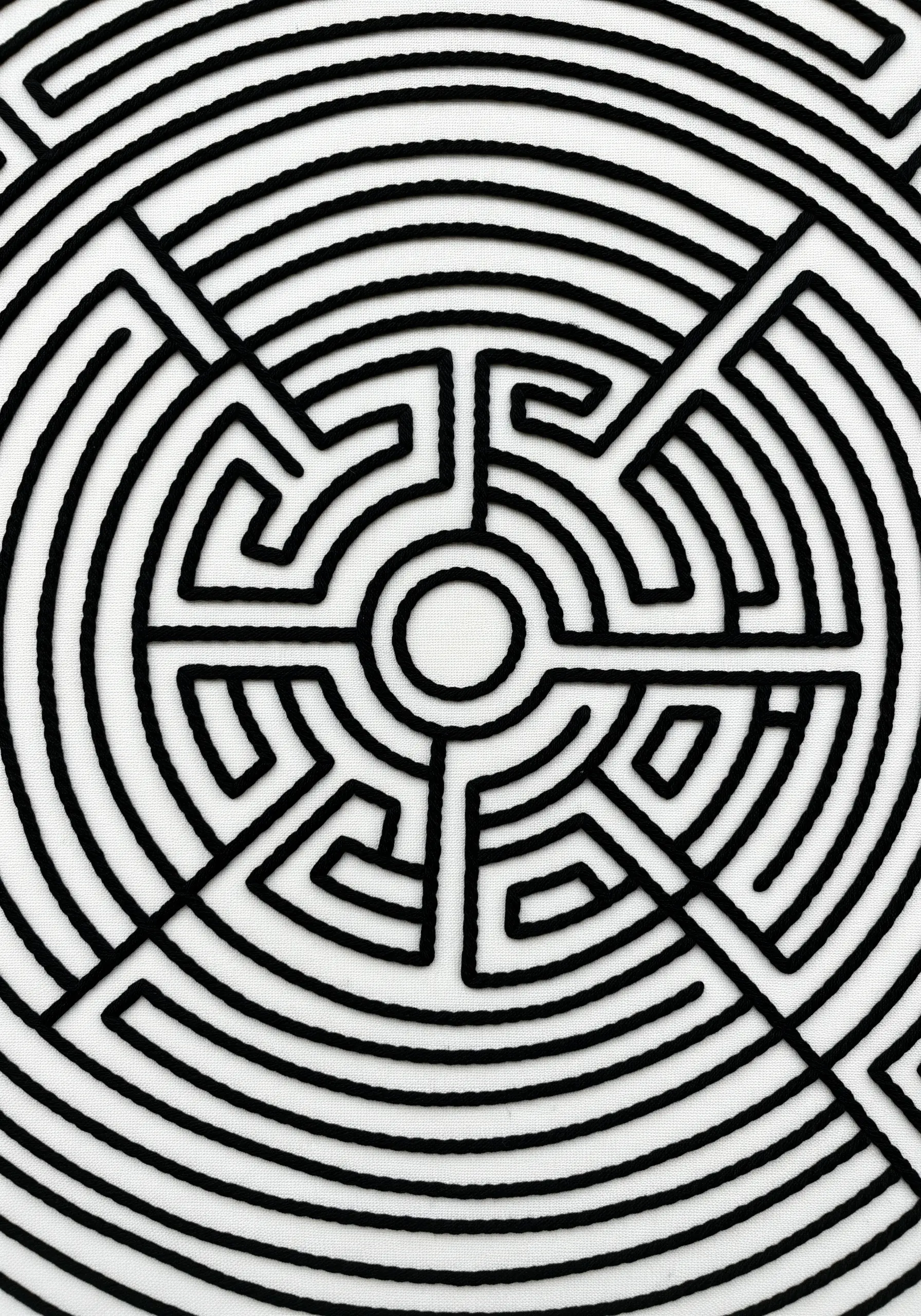 A bold, black labyrinth pattern stitched with thick thread on a plain white background.