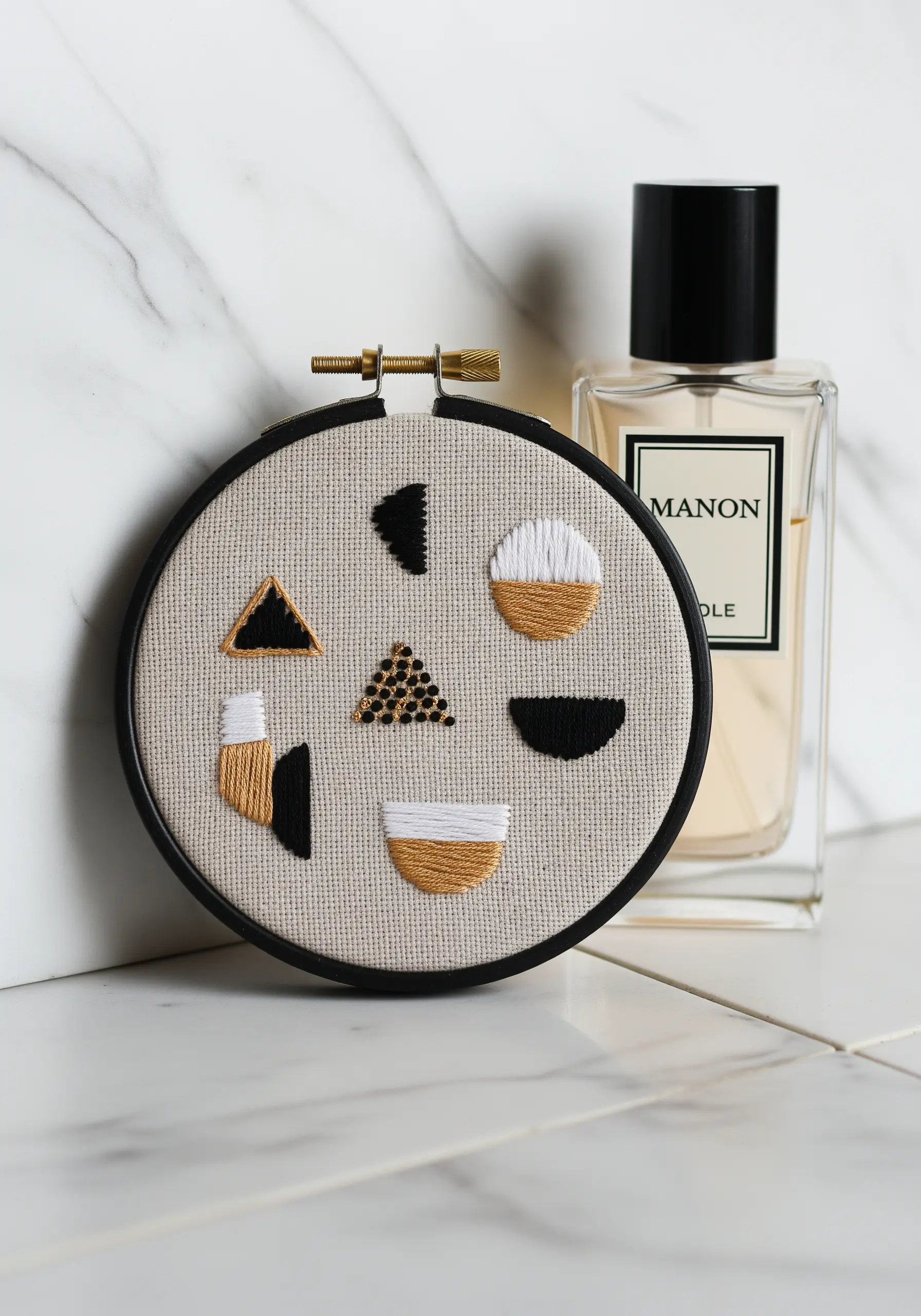 Small embroidery hoop with a balanced composition of abstract geometric shapes in black, white, and gold.
