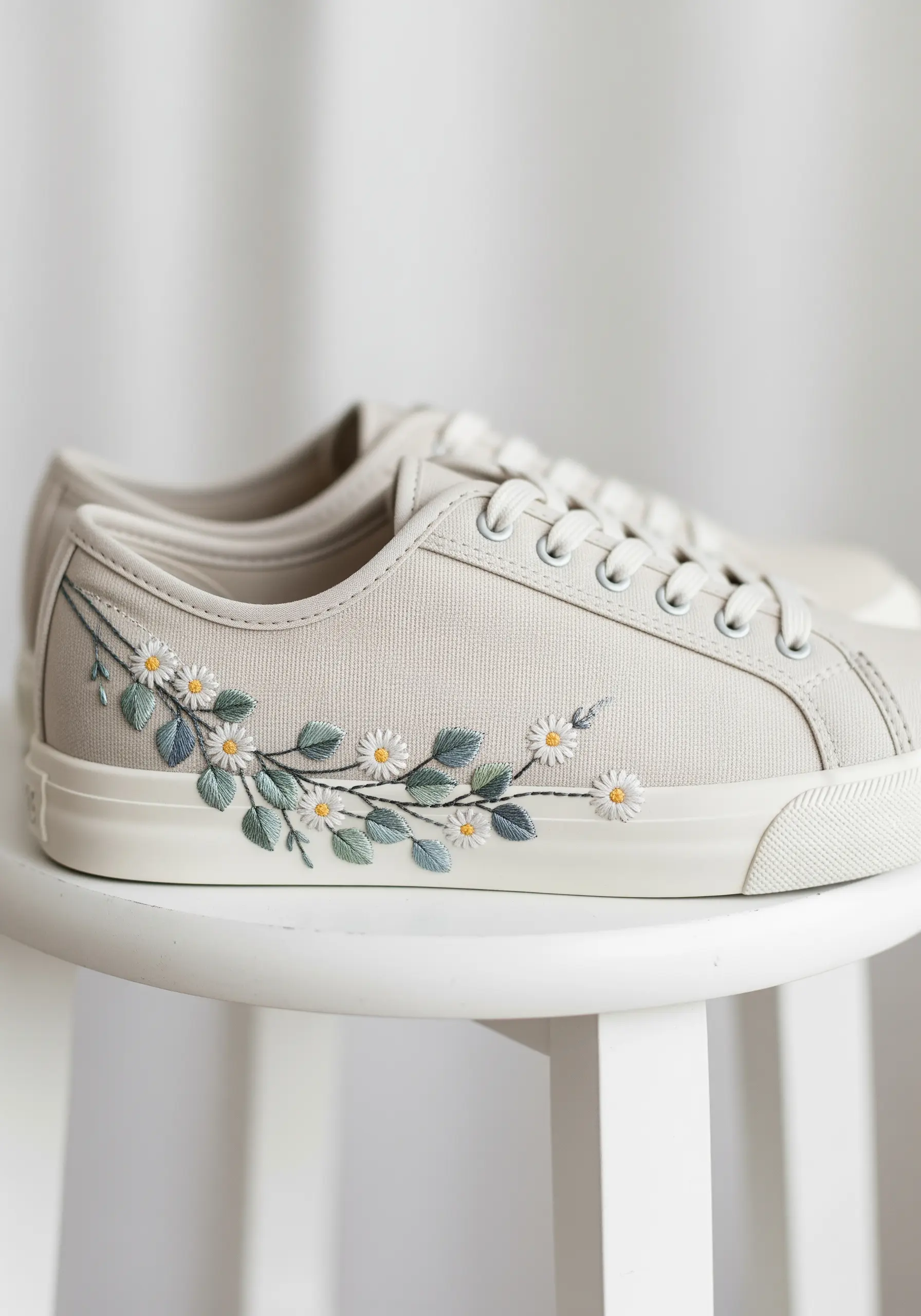 A delicate spray of daisies and sage leaves embroidered on light gray canvas sneakers.