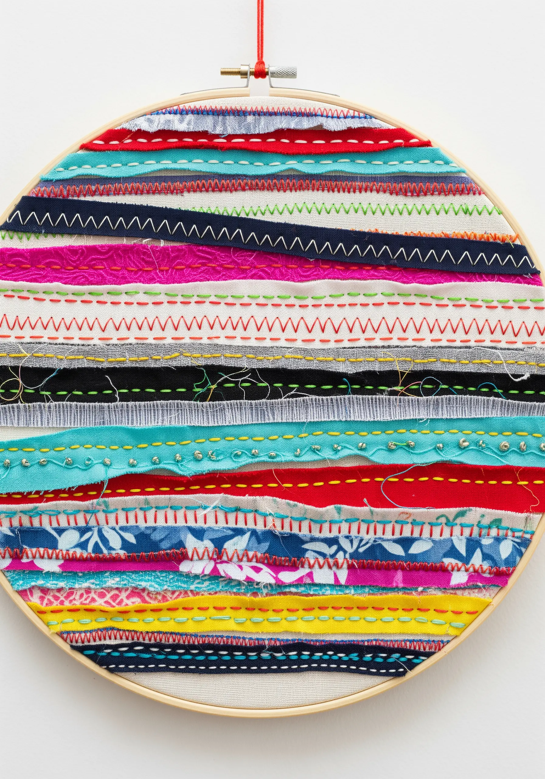 Hoop art made from horizontal strips of colorful fabric and decorative stitches.