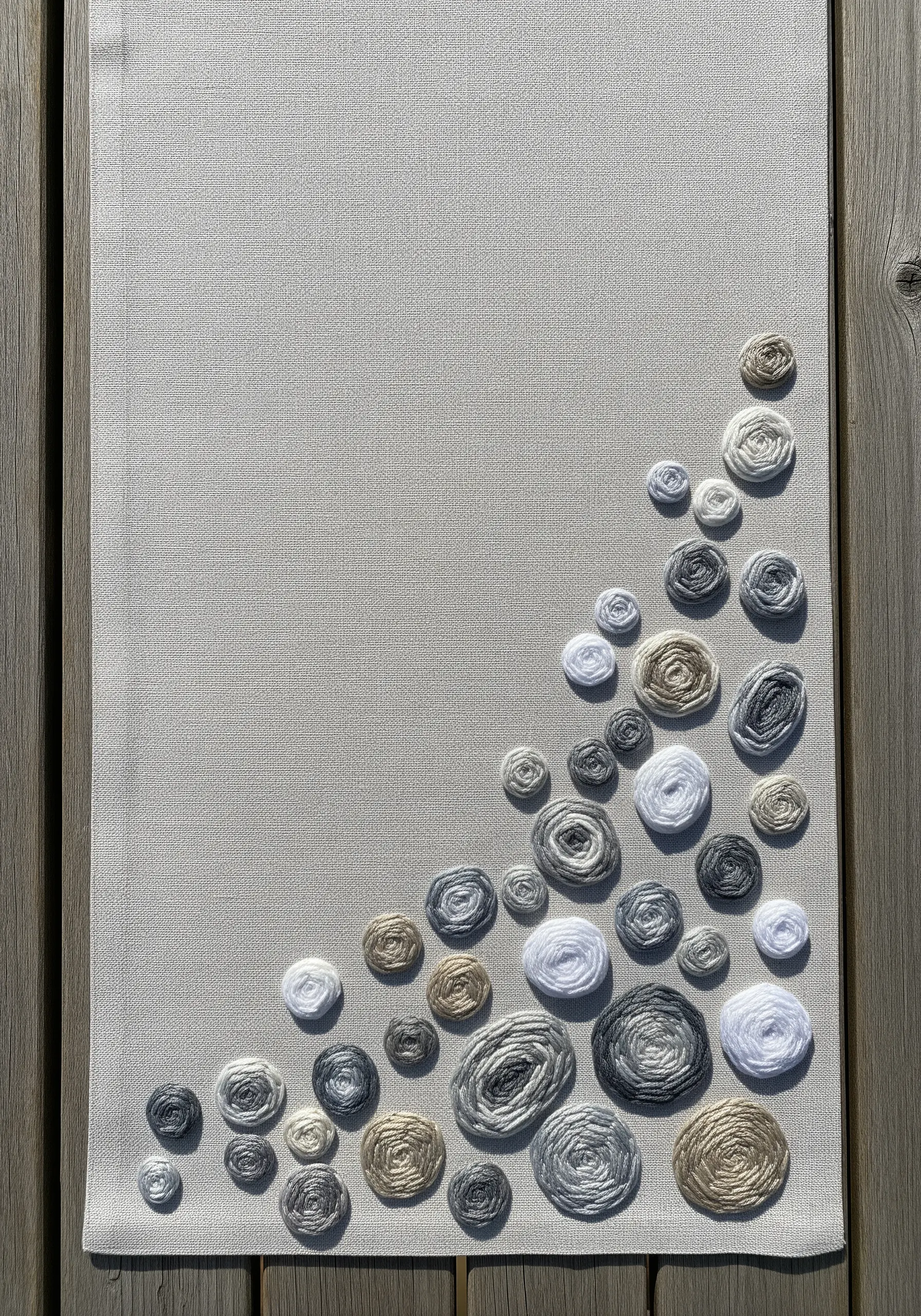 A minimalist table runner decorated with an asymmetrical cluster of woven wheel stitches in neutral tones.