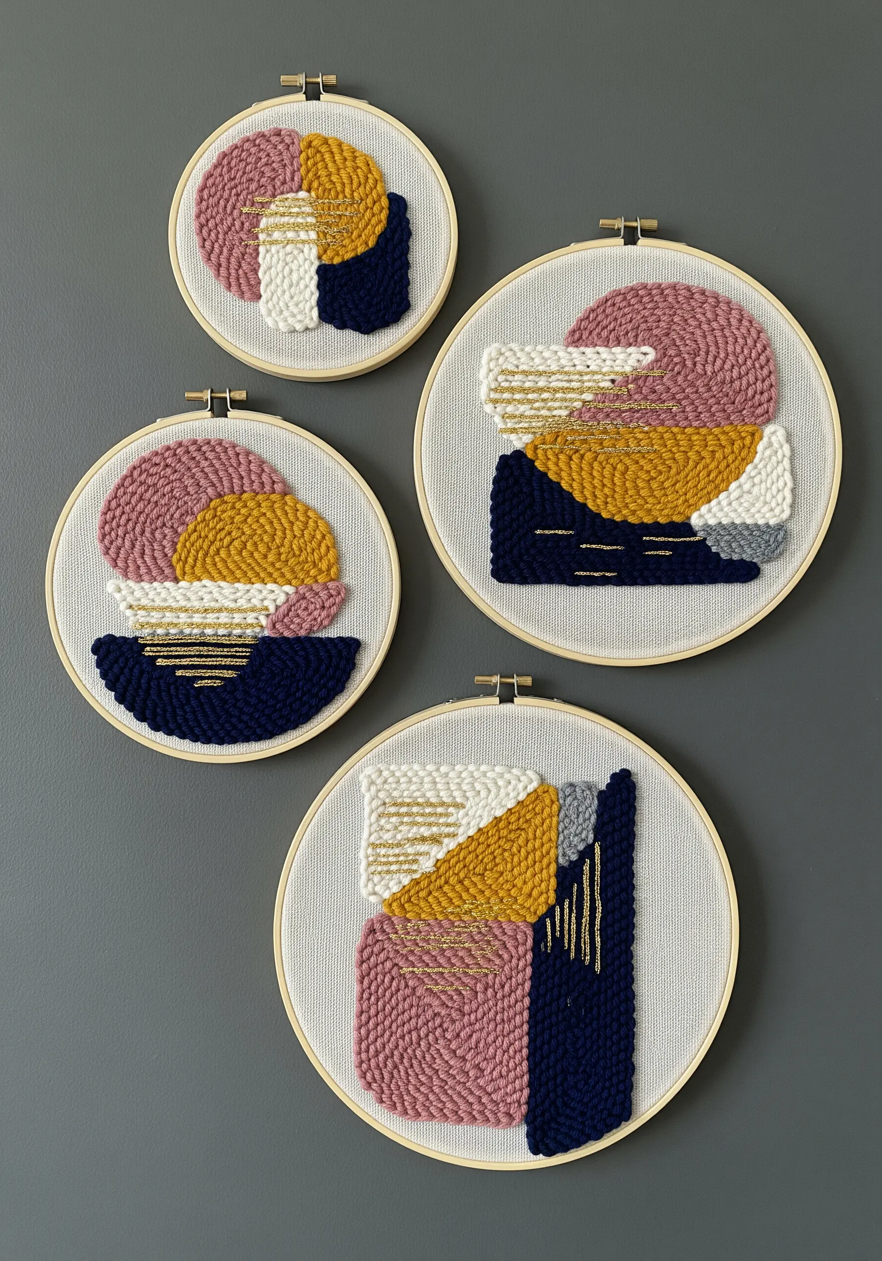 Four punch needle hoops with abstract geometric shapes in pink, yellow, and navy blue.