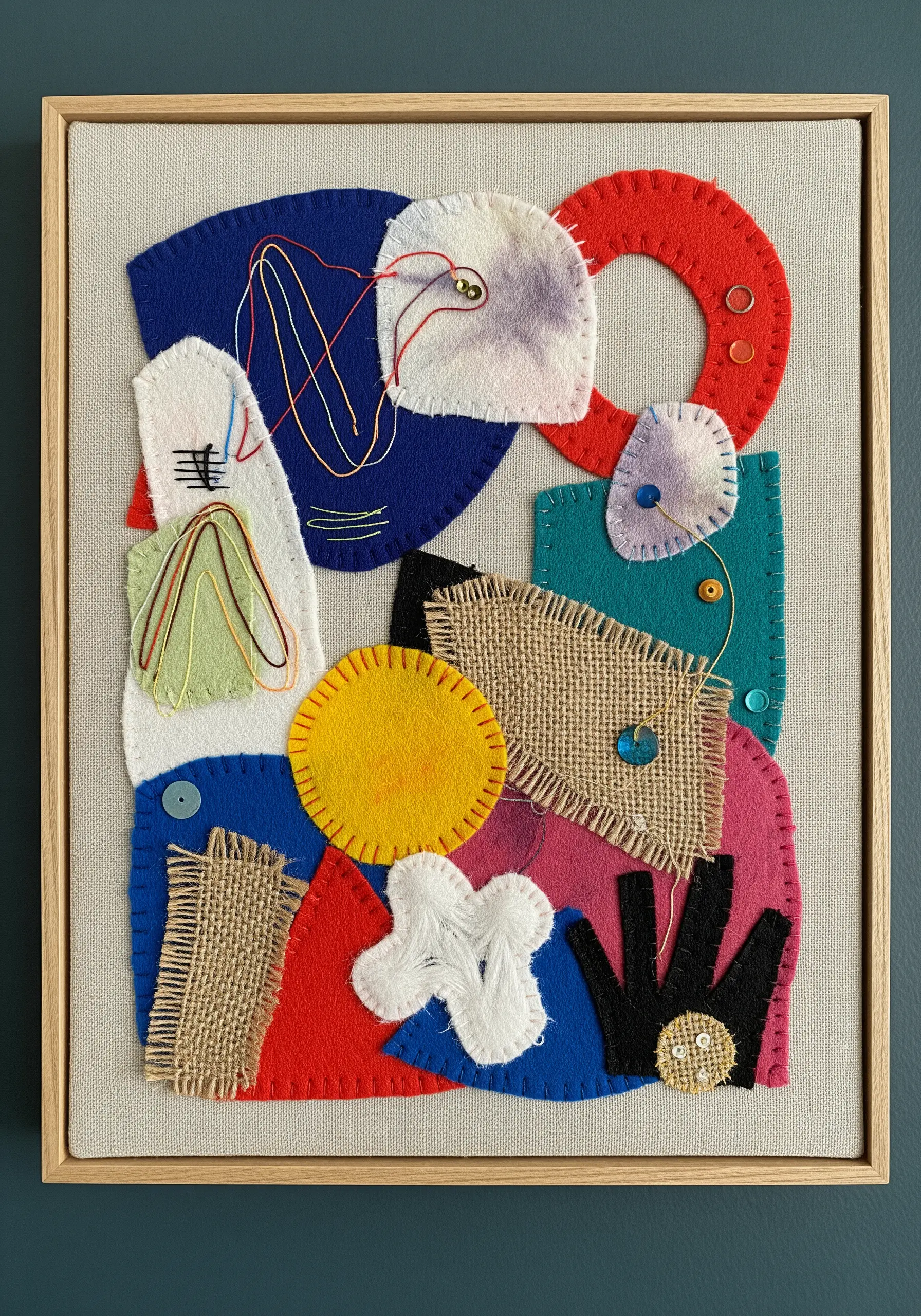 Framed abstract collage of layered felt, burlap, and fabric scraps with simple hand stitches.
