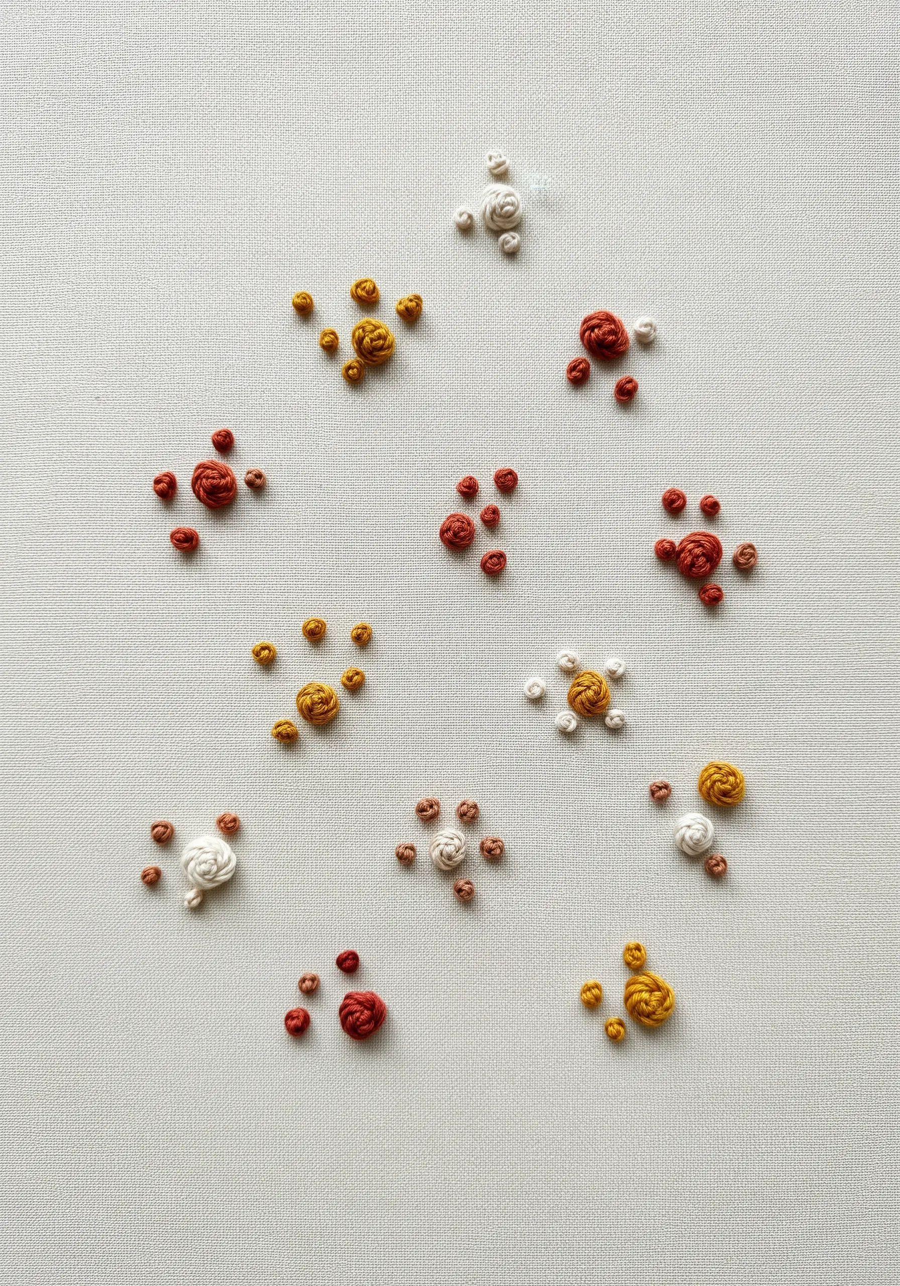 Scattered clusters of French and bullion knots in warm tones on a neutral background.