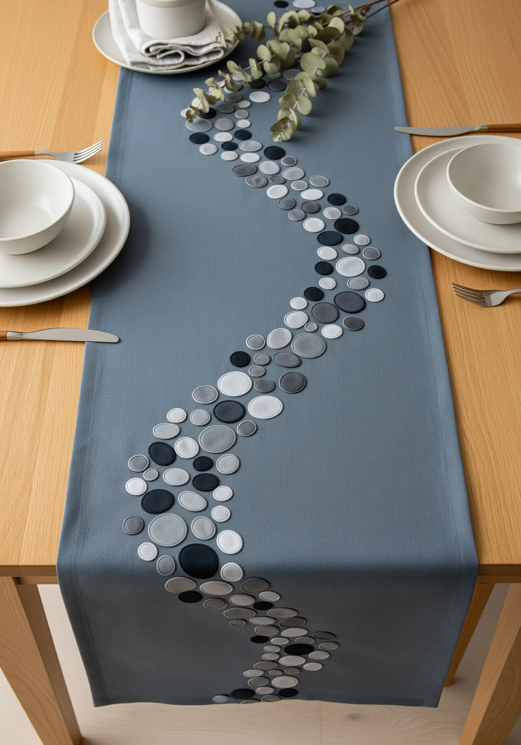 A blue-gray table runner with an abstract, winding path of embroidered satin-stitch pebbles.