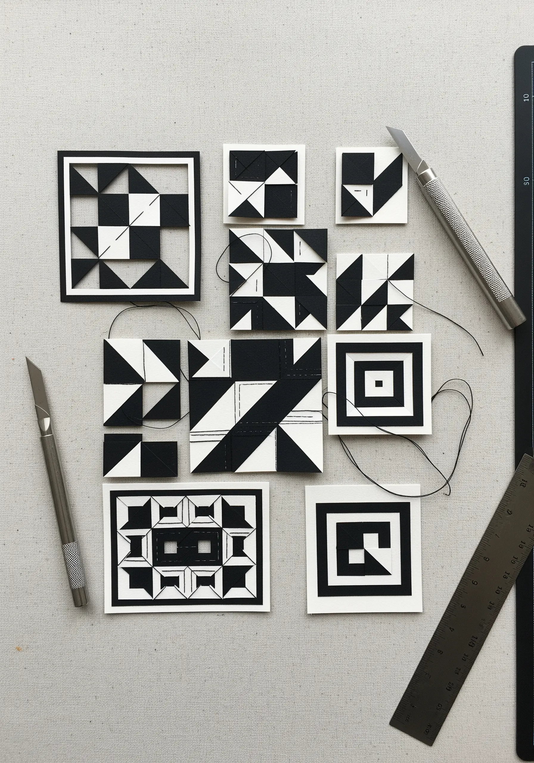 Black and white geometric paper tiles connected with thin black and white threads.