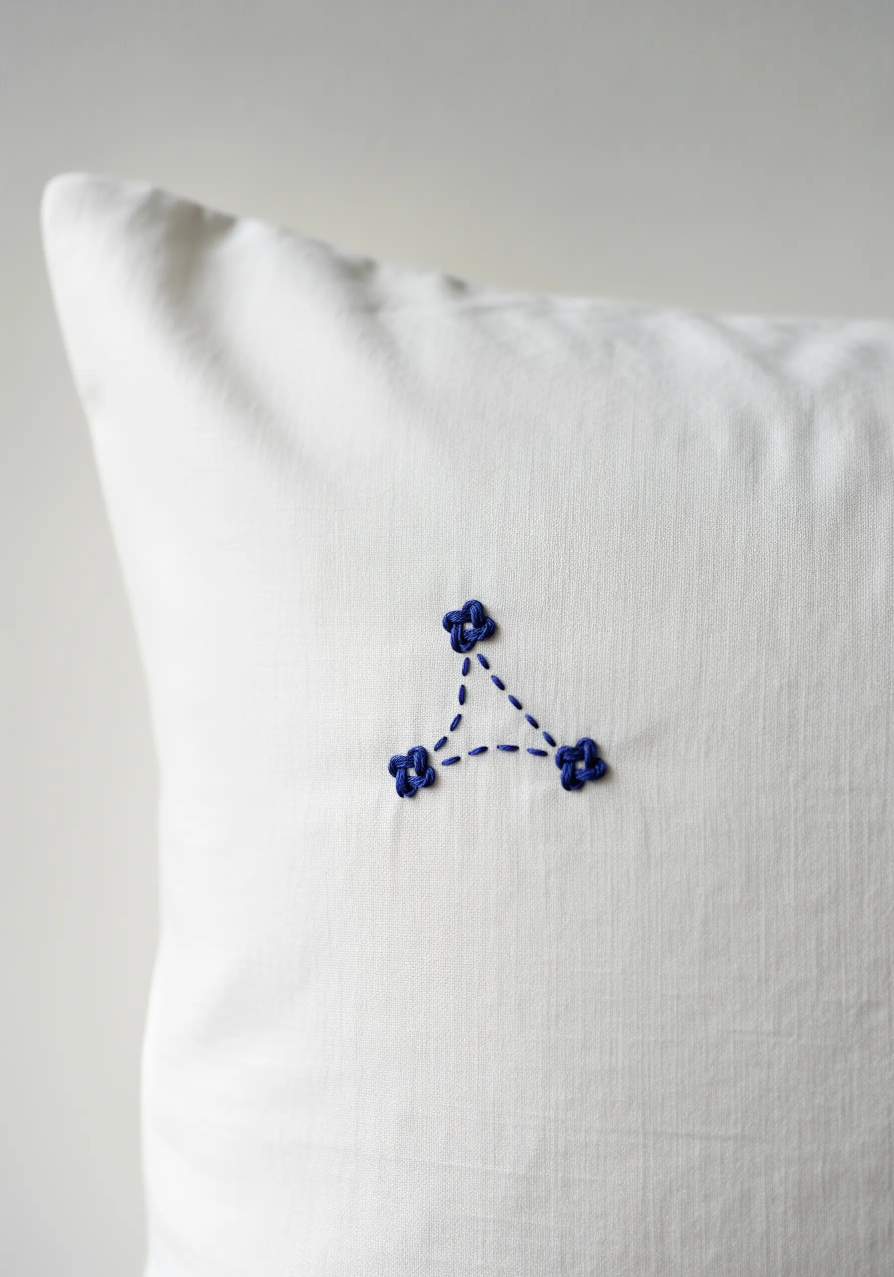 A small, triangular constellation embroidered with blue French knots on a white pillow.