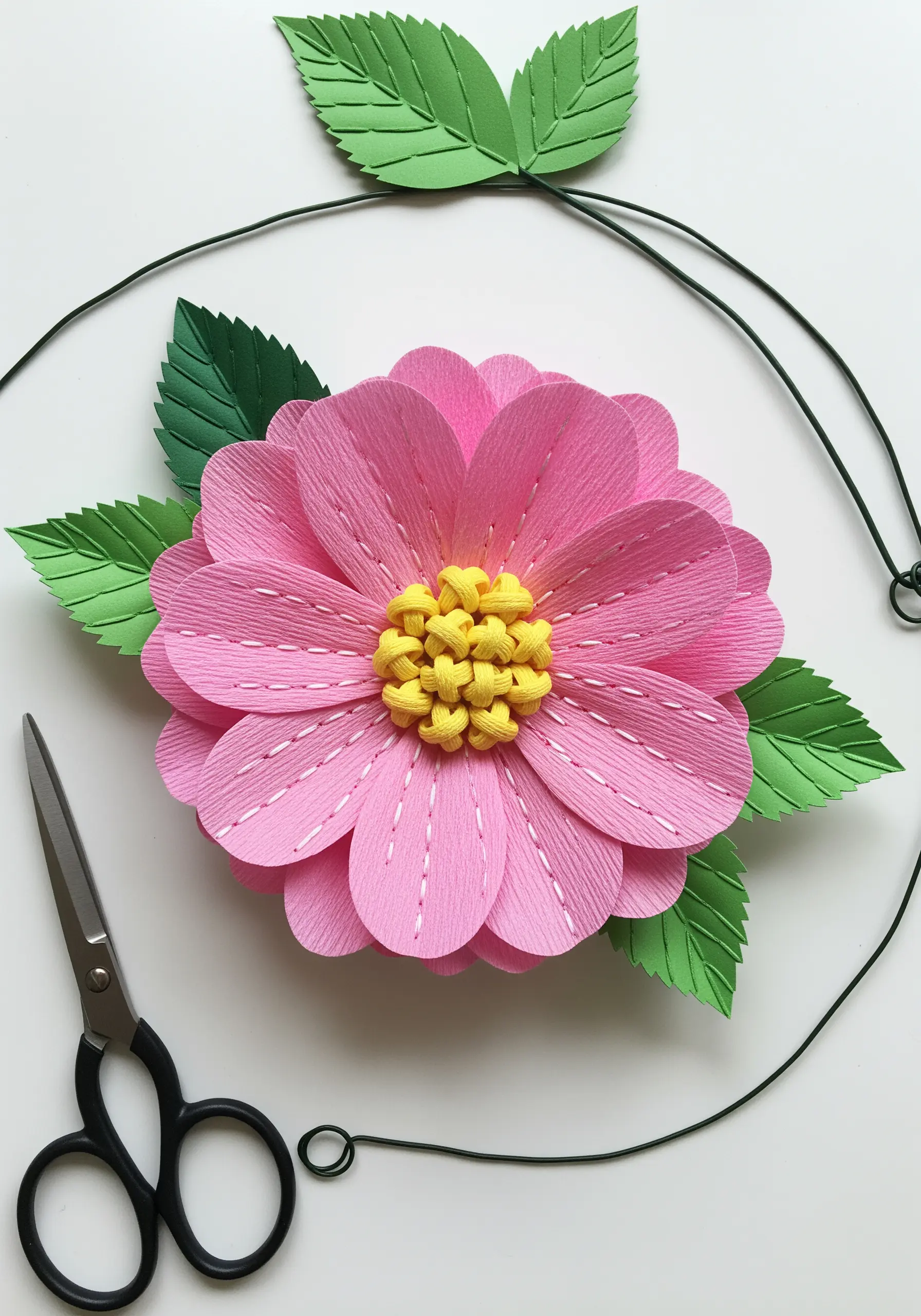 A 3D pink paper flower with white running stitches on its petals and a yellow knotted center.
