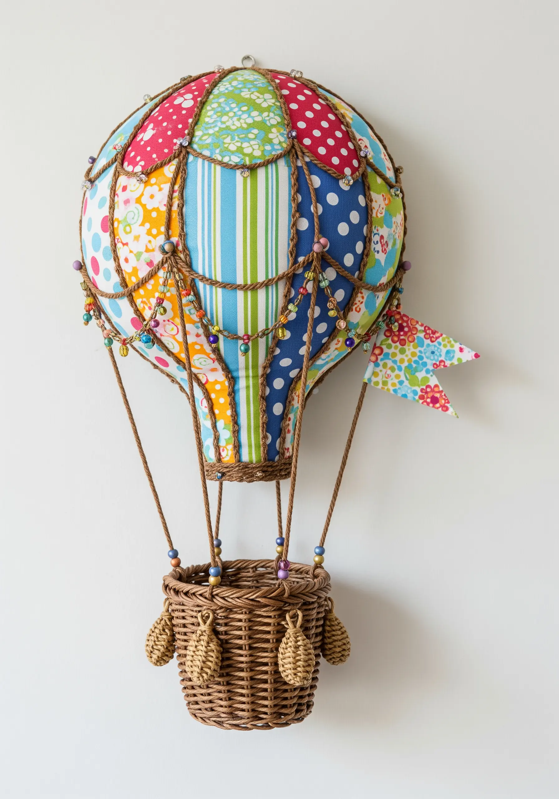 A 3D hot air balloon wall decoration made from patchwork fabric, a wicker basket, and beads.
