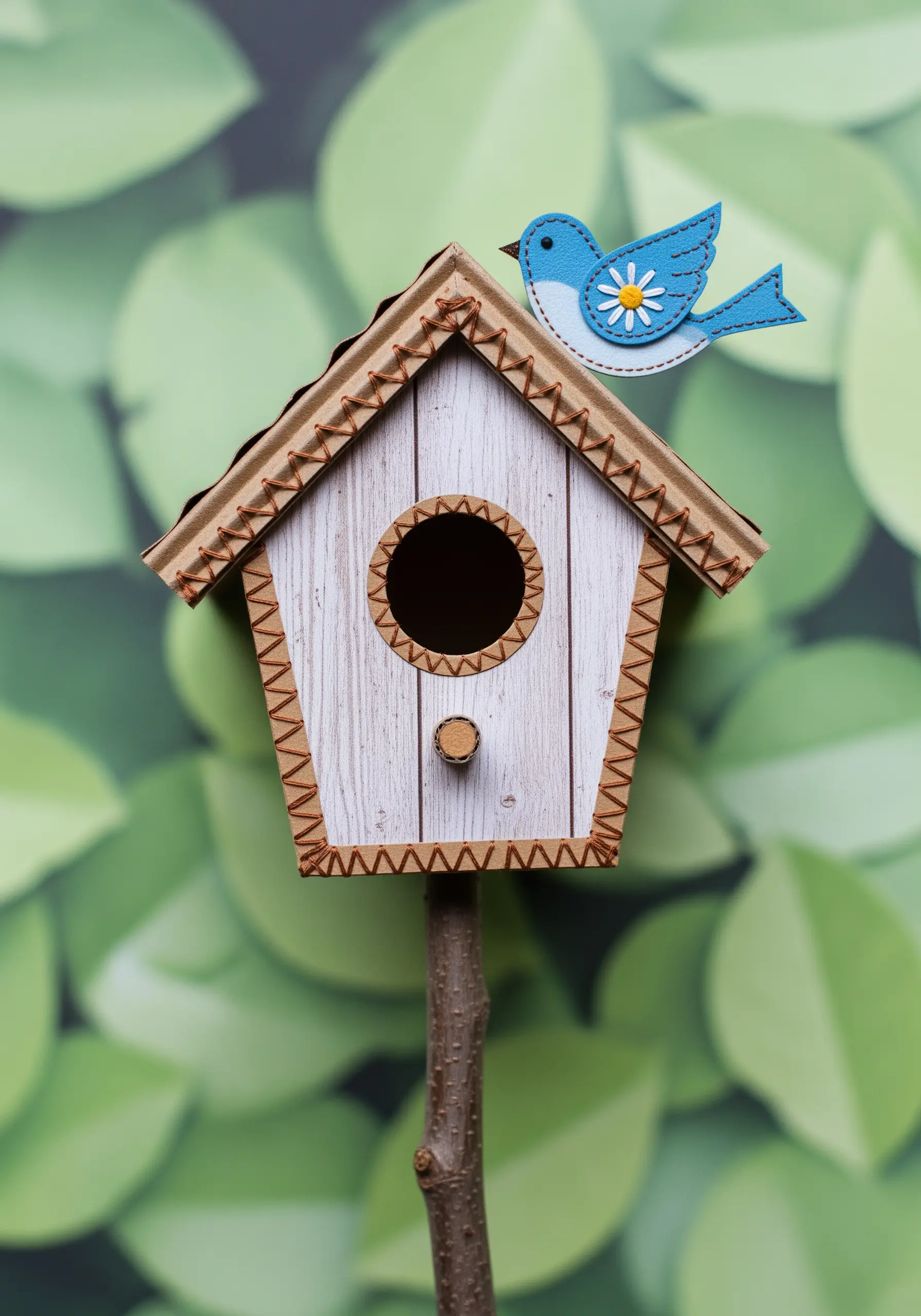 A 3D paper birdhouse collage where the edges are joined with a decorative brown blanket stitch.