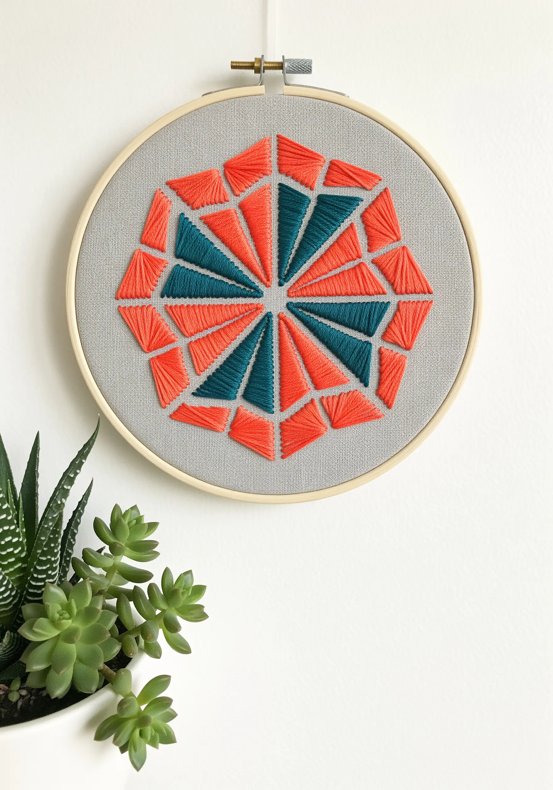 A geometric mandala with interlocking triangles in vibrant orange and teal satin stitch.