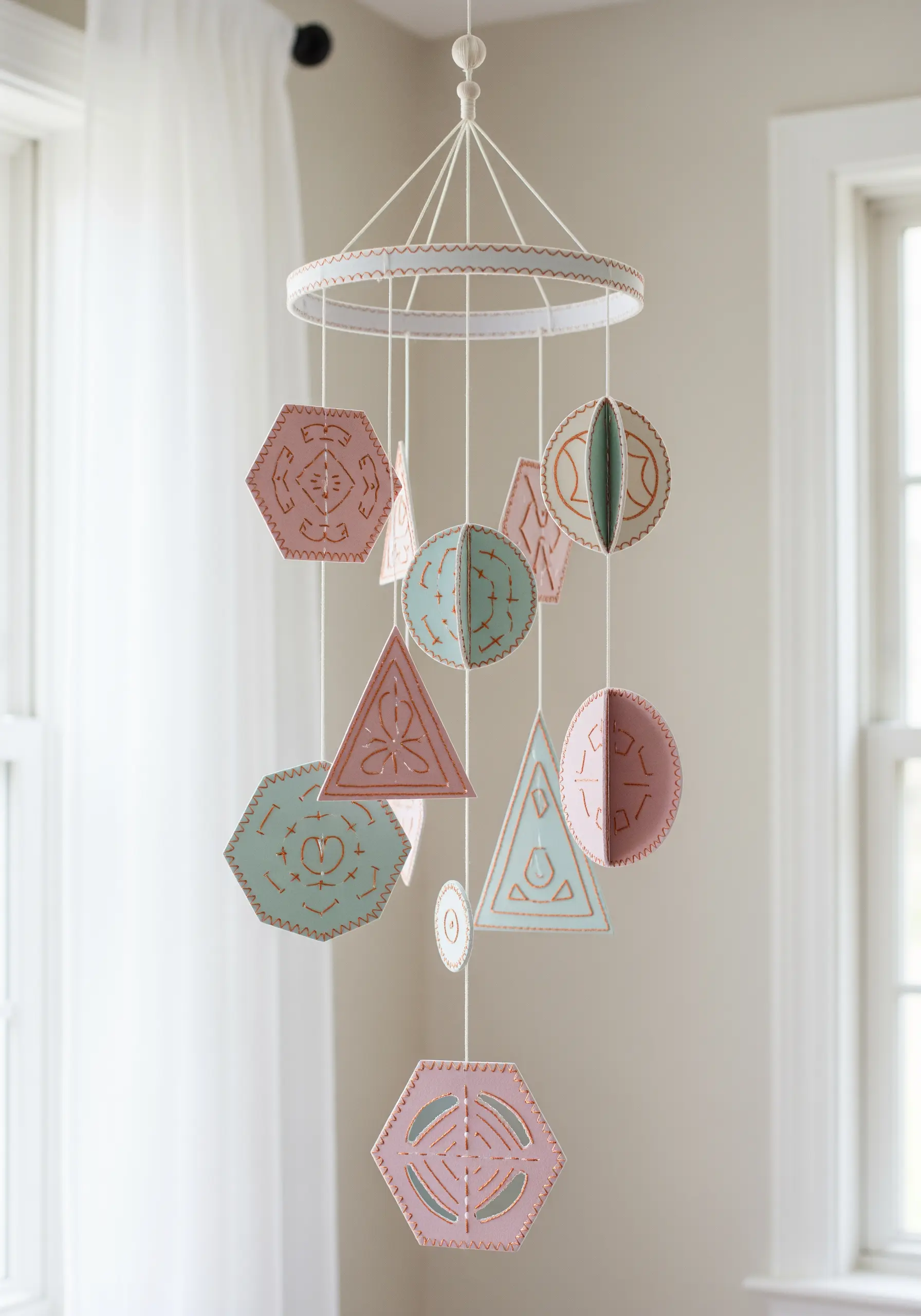 A baby mobile made from geometric paper shapes in pink and teal with stitched edges.