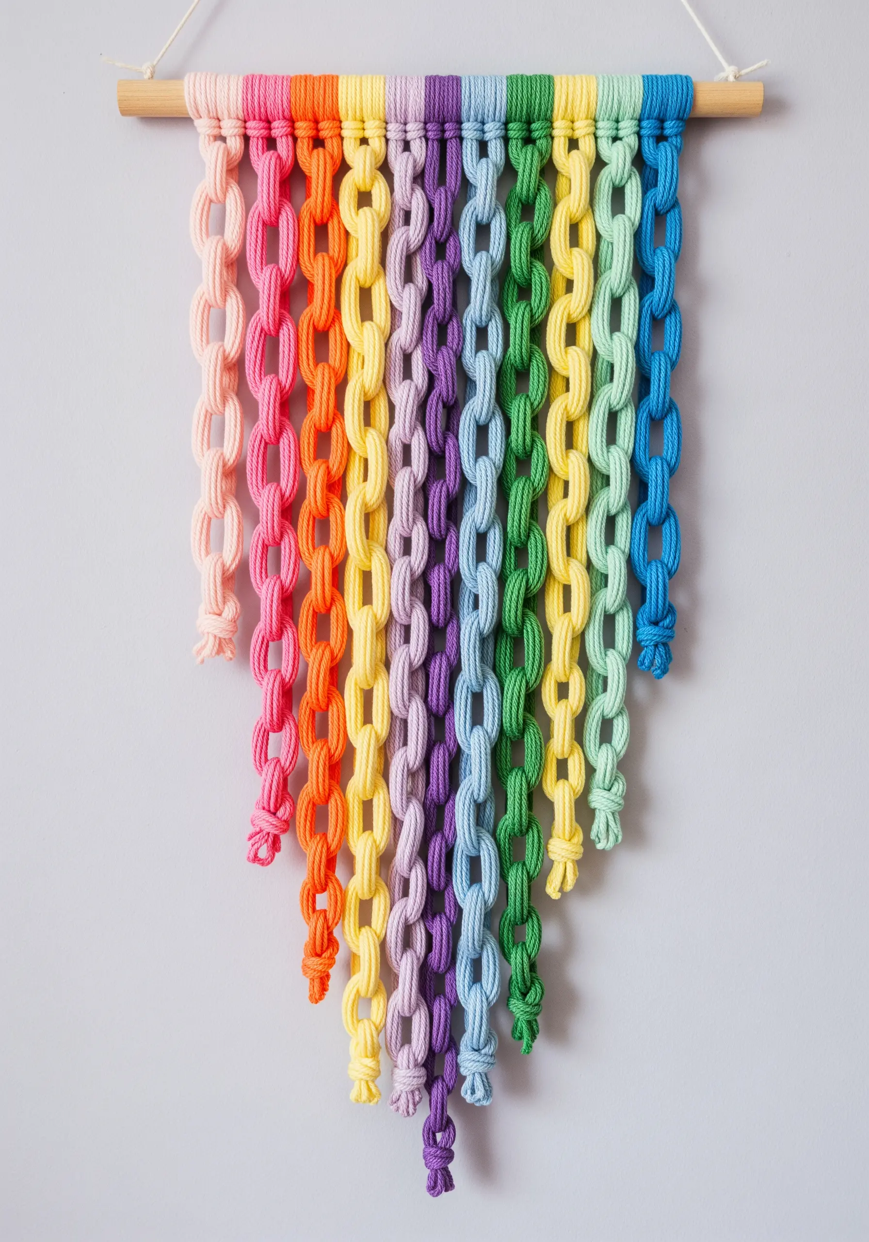 A rainbow wall hanging made of interconnected macrame chain links hanging from a dowel.