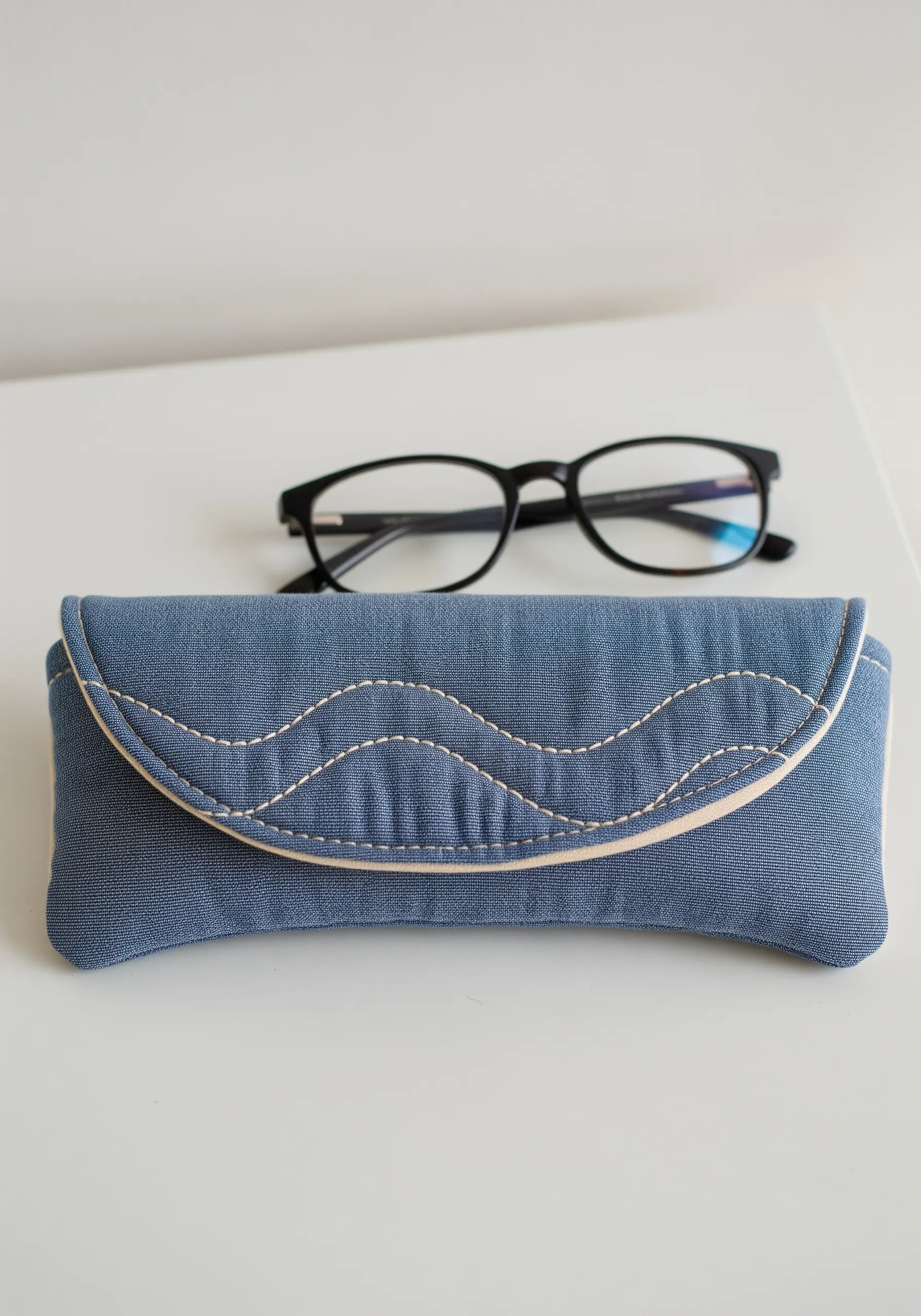 A padded blue fabric glasses case with decorative stitching and cream piping.