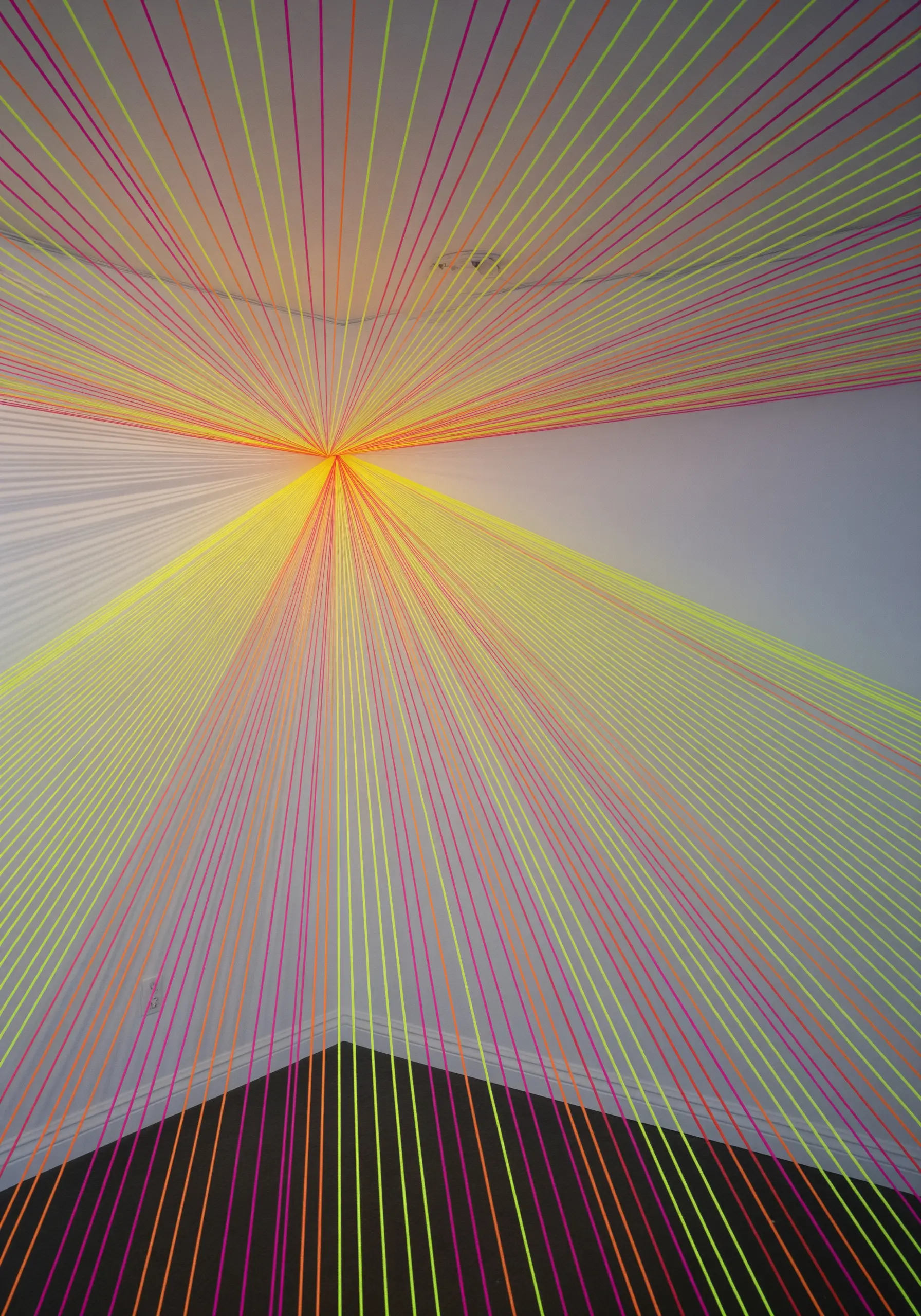 A corner of a room filled with a neon string art installation radiating from the ceiling.