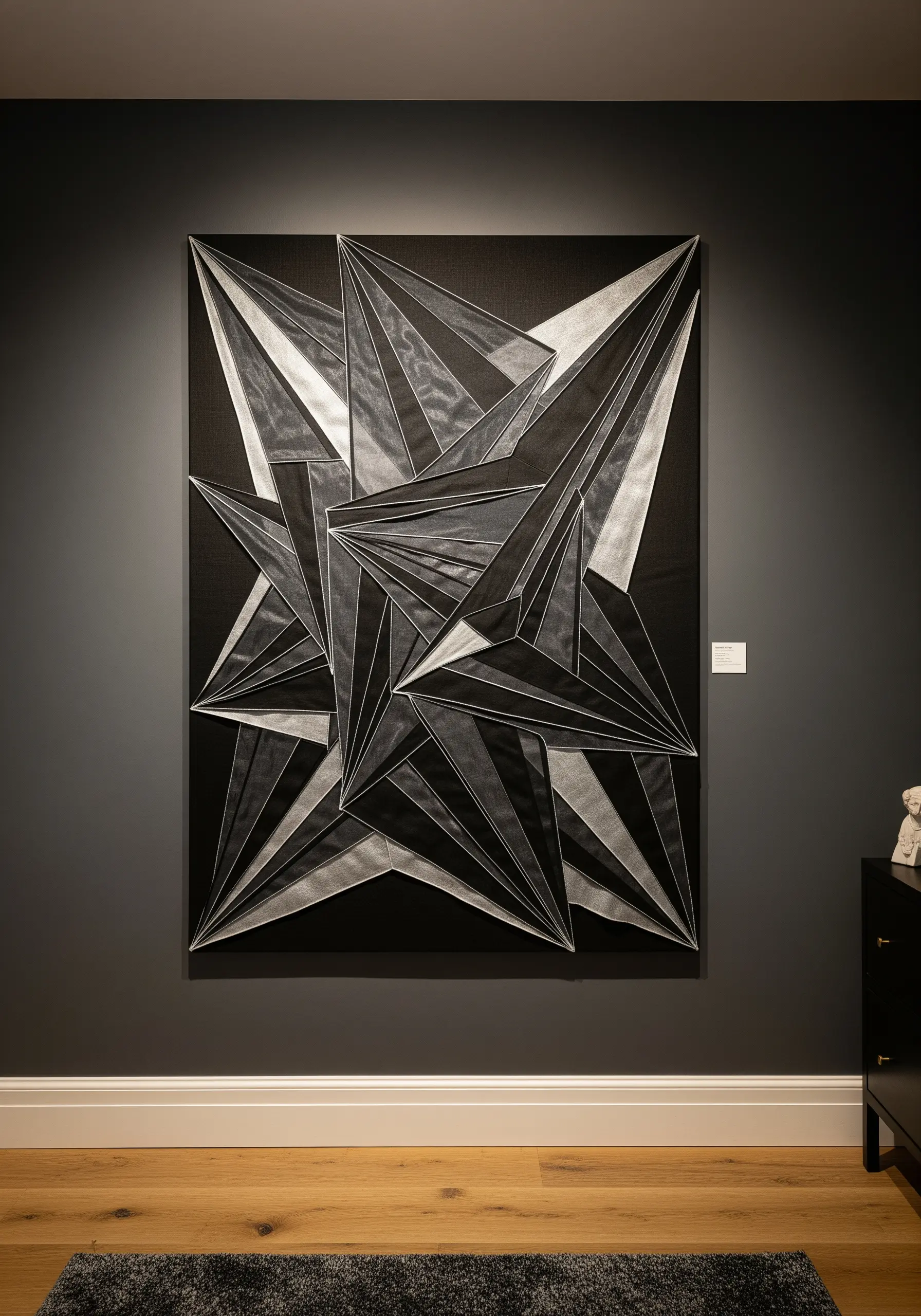 A large, abstract geometric artwork on a black canvas using layered white and grey sheer fabrics.