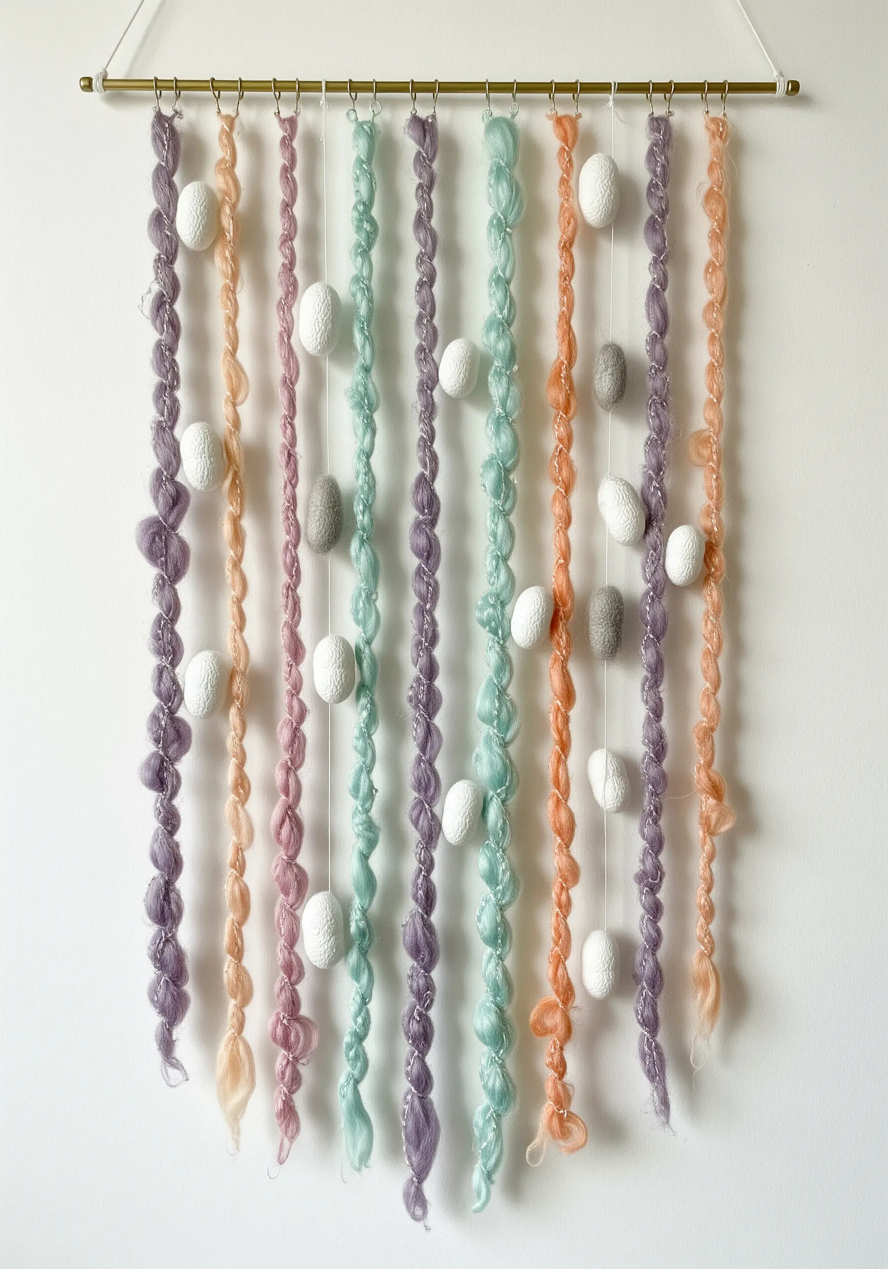 A delicate wall garland made of pastel-colored spun yarn and small white felted eggs.