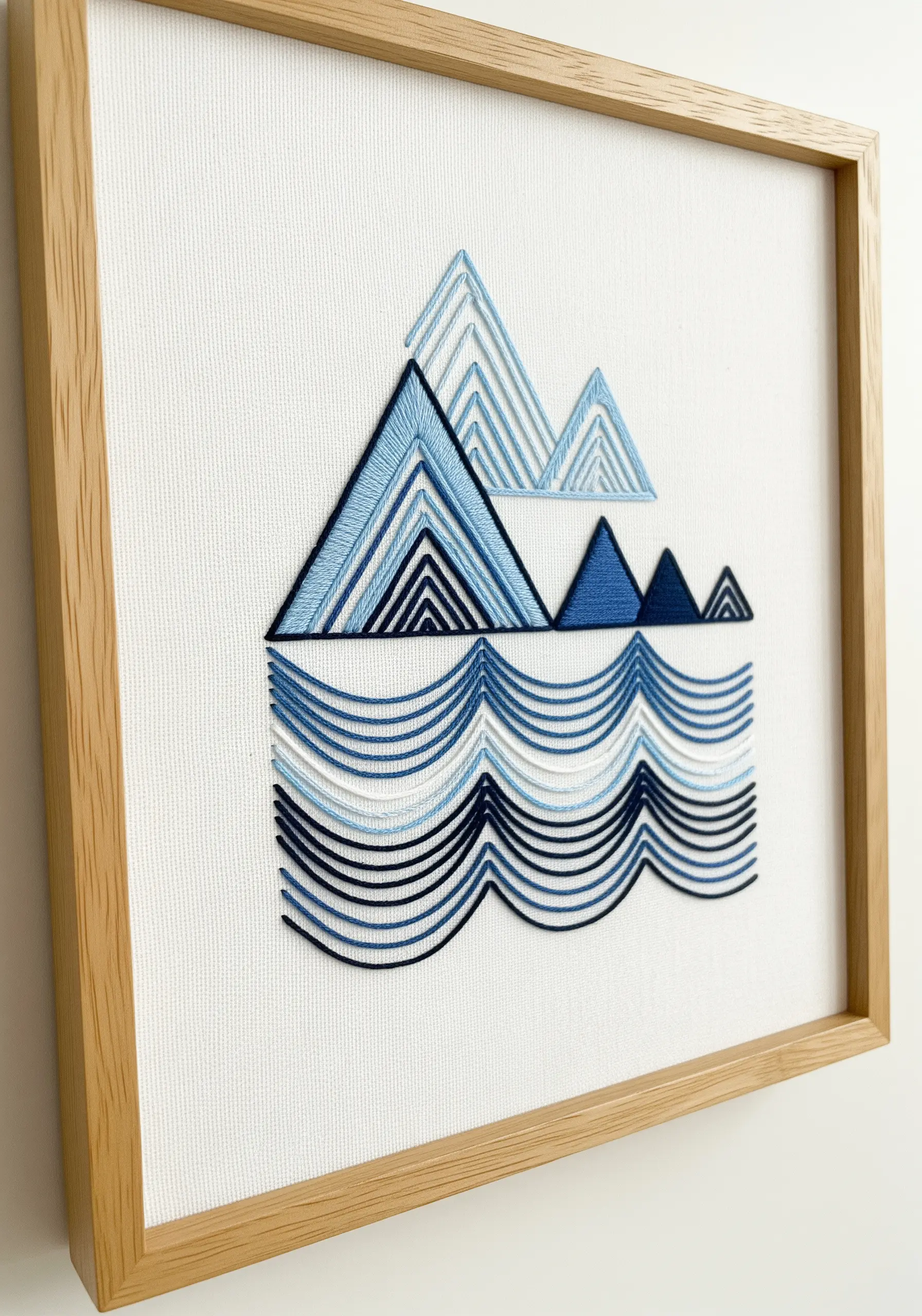 Geometric embroidery of mountains and waves using blue and white satin stitch blocks.