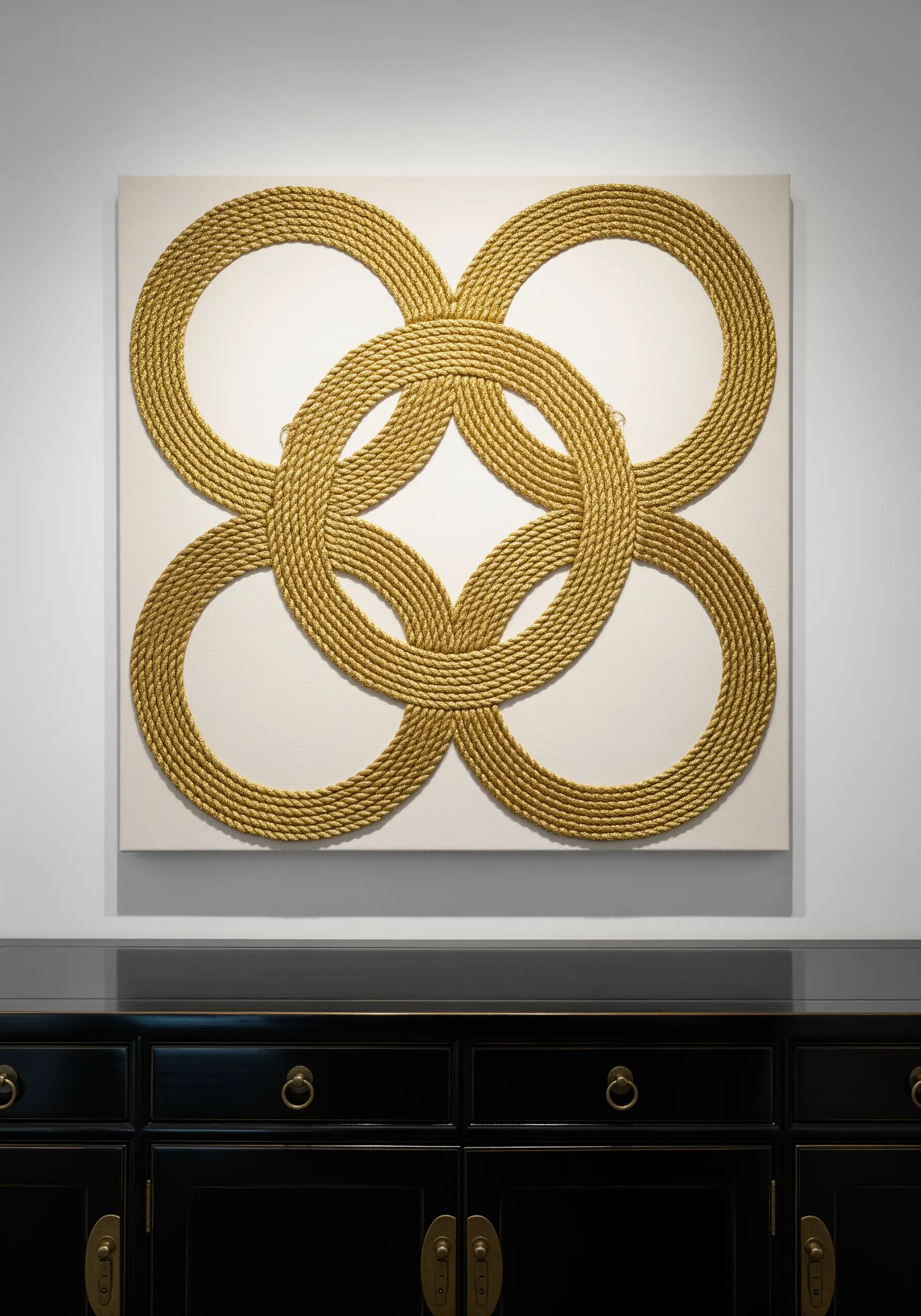 Wall art featuring four interlocking rings made from thick, couched gold metallic rope on white canvas.