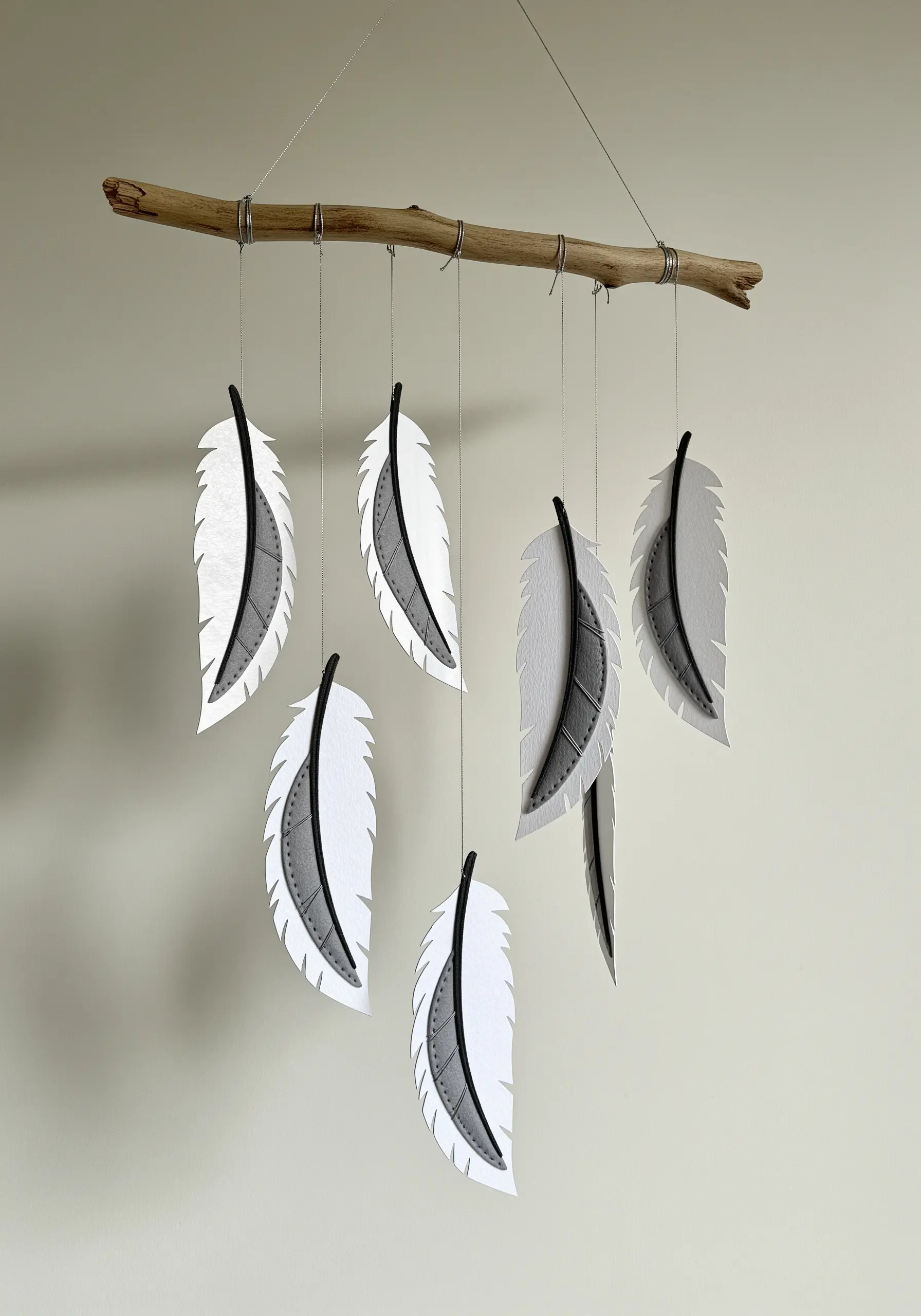 A wall mobile featuring hanging feathers made from stitched white and gray paper.