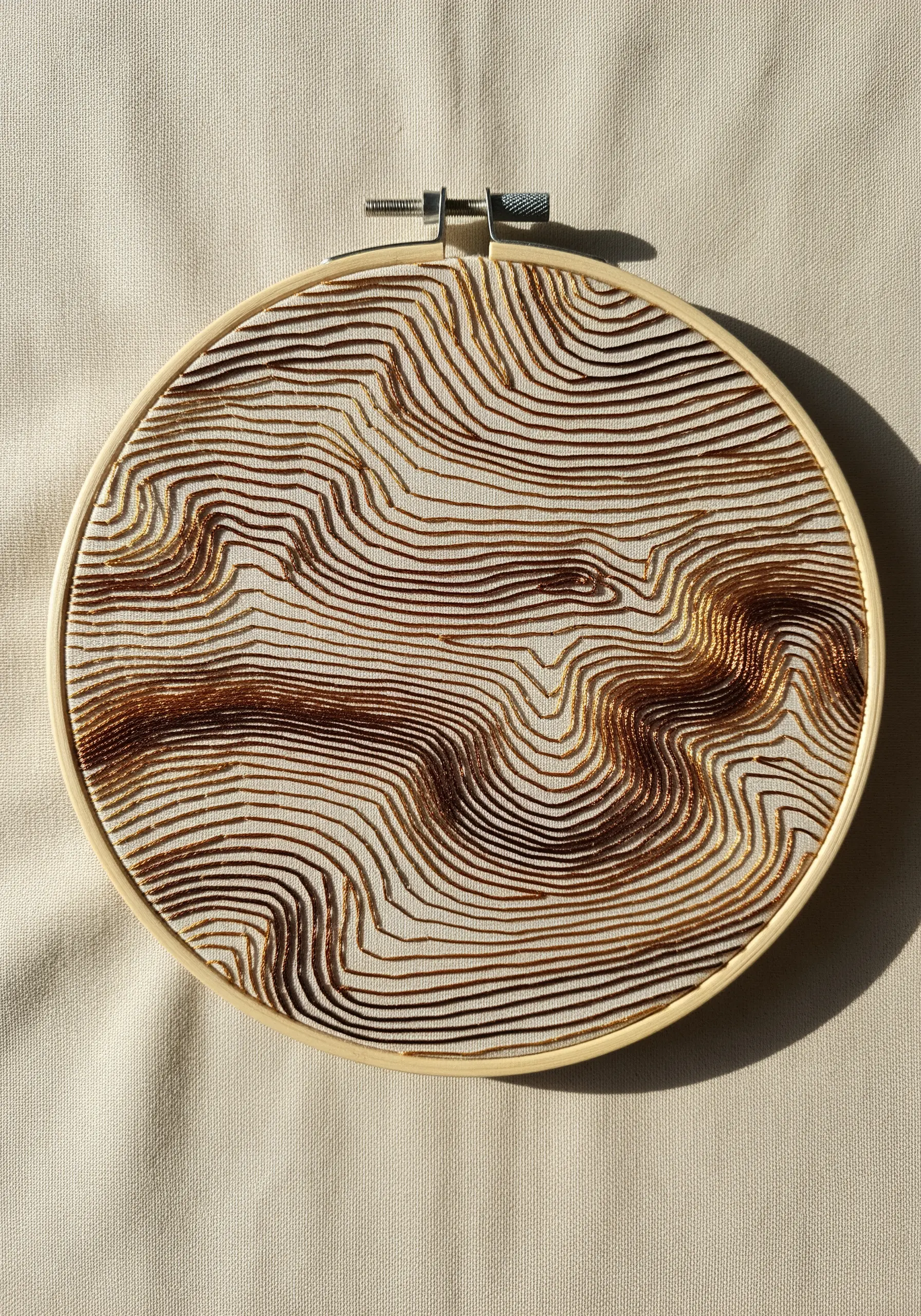 Dense, parallel contour lines in bronze metallic thread creating a topographic effect.