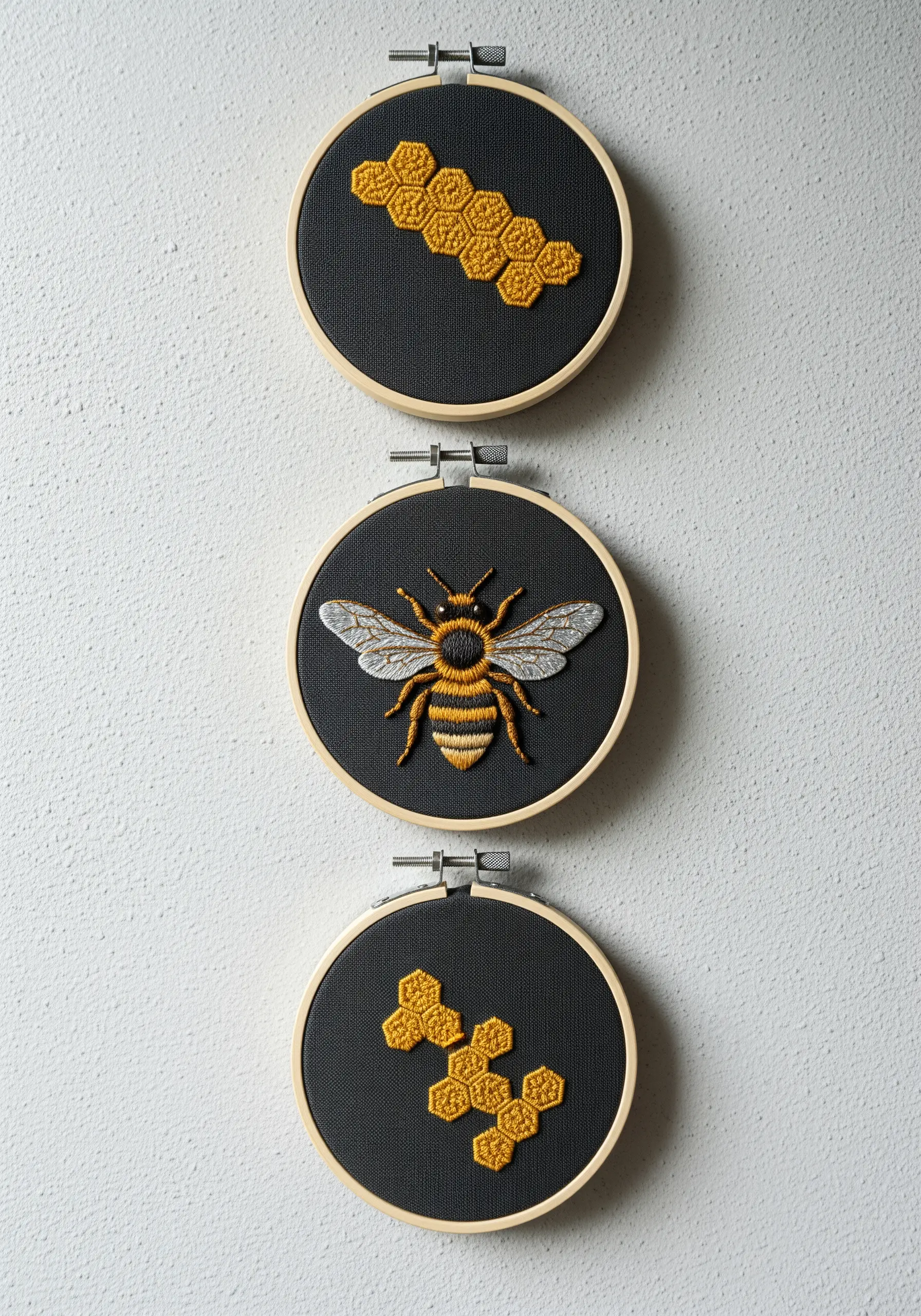 A triptych of embroidery hoops on a white wall featuring a bee and honeycombs.