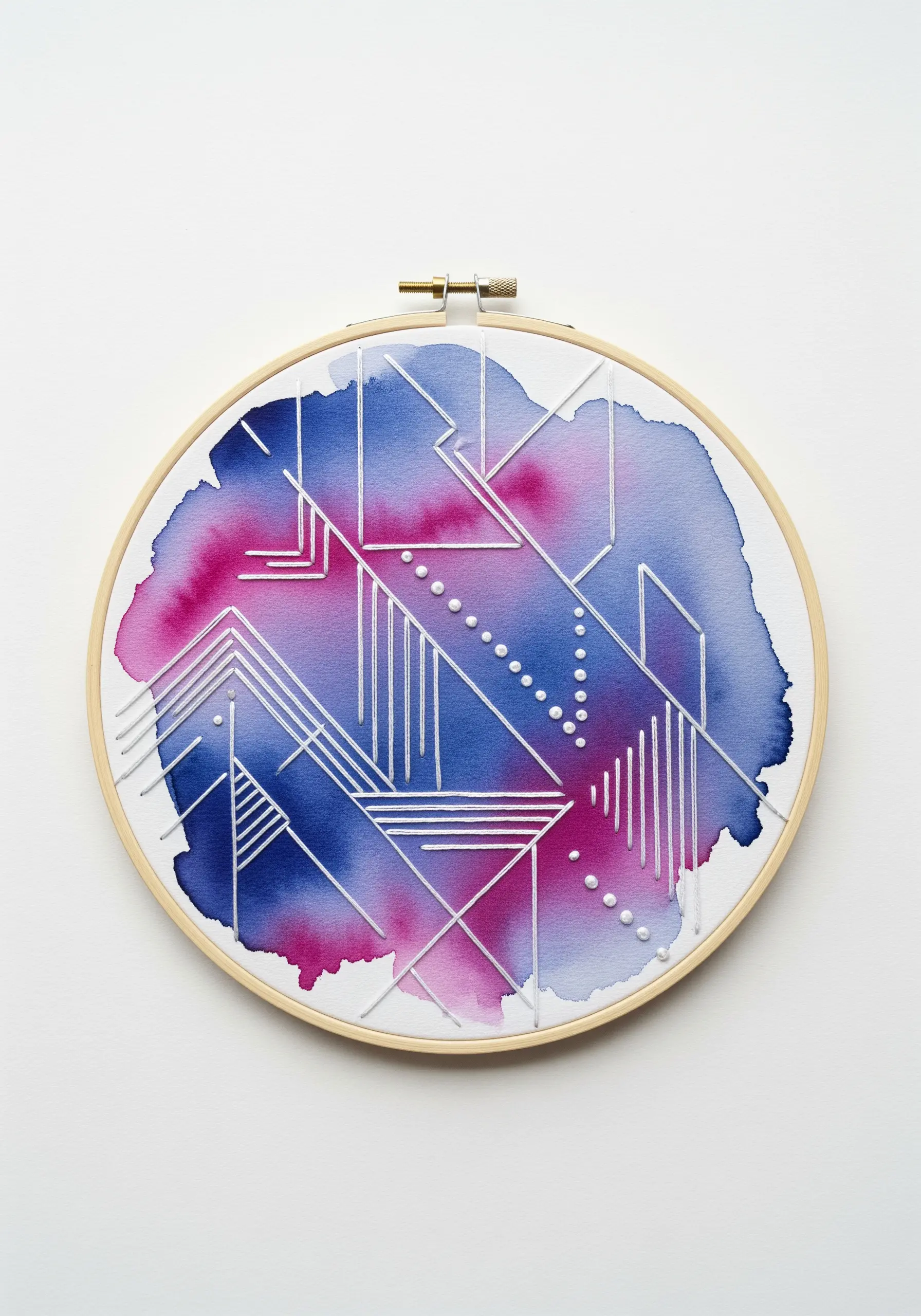 White thread geometric line art and French dots embroidered over a pink and blue watercolor wash.