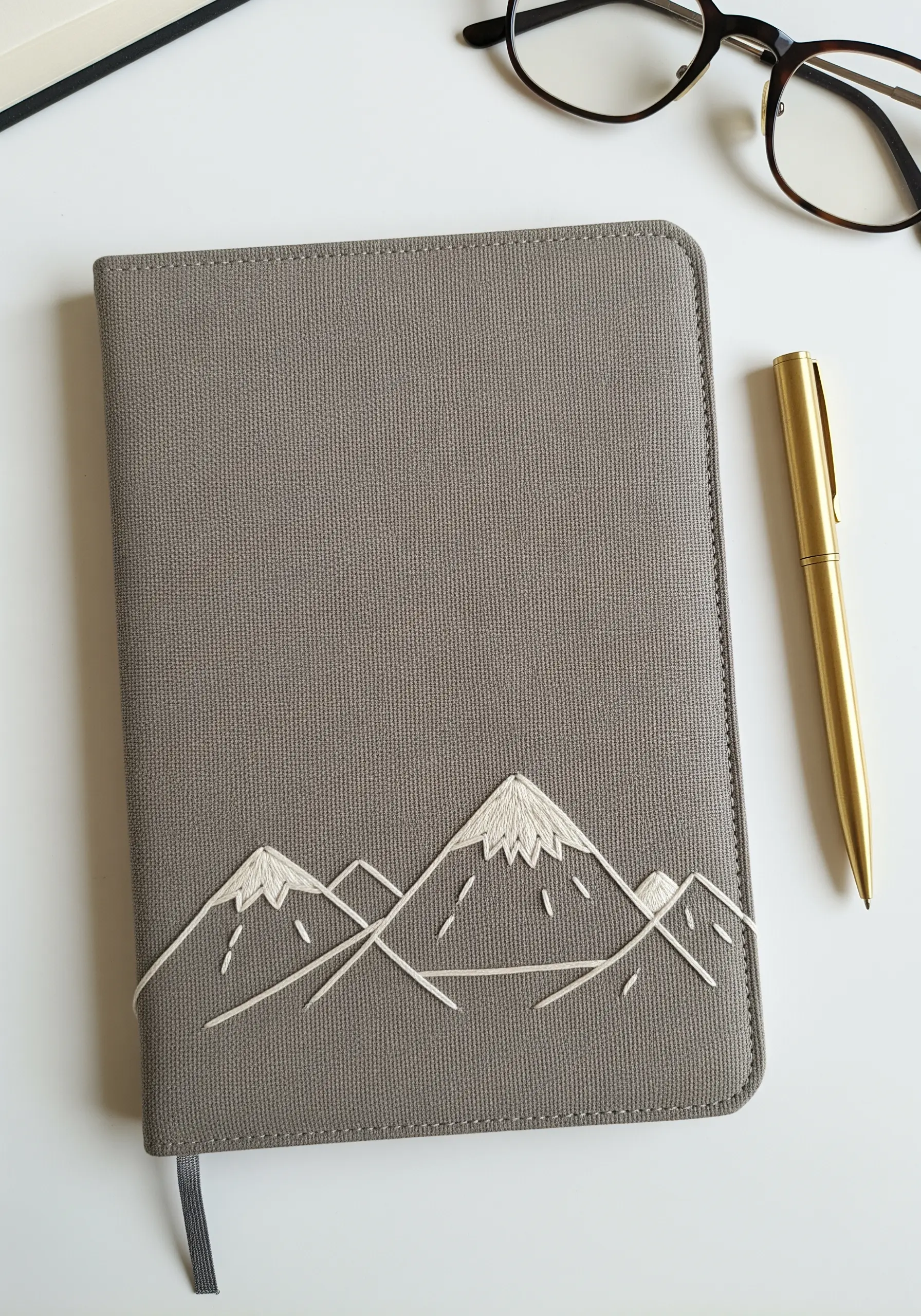 Line art mountains with satin-stitched snow caps embroidered on a grey journal cover.
