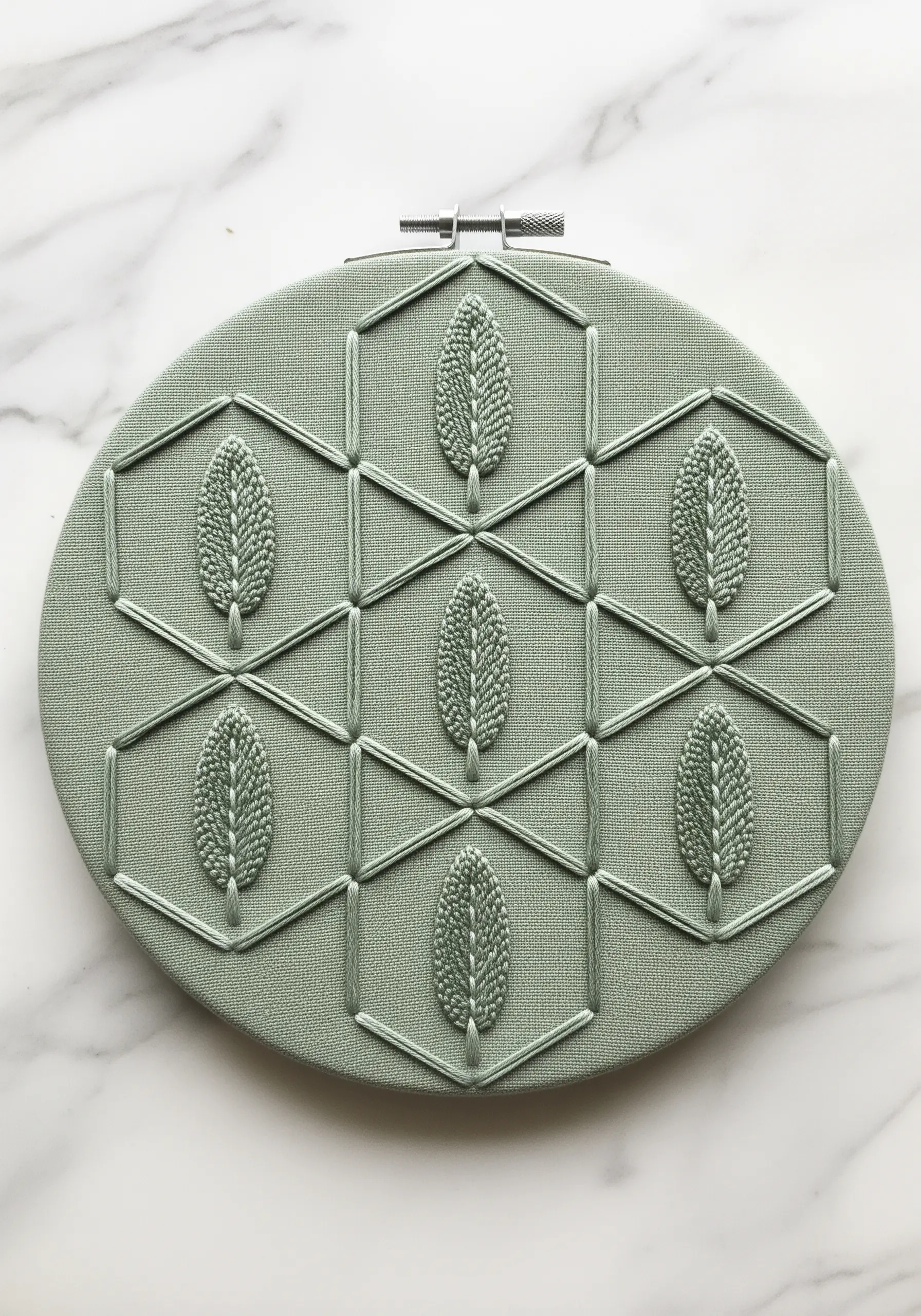Monochrome embroidery of sage leaves within a geometric honeycomb pattern on sage green fabric.