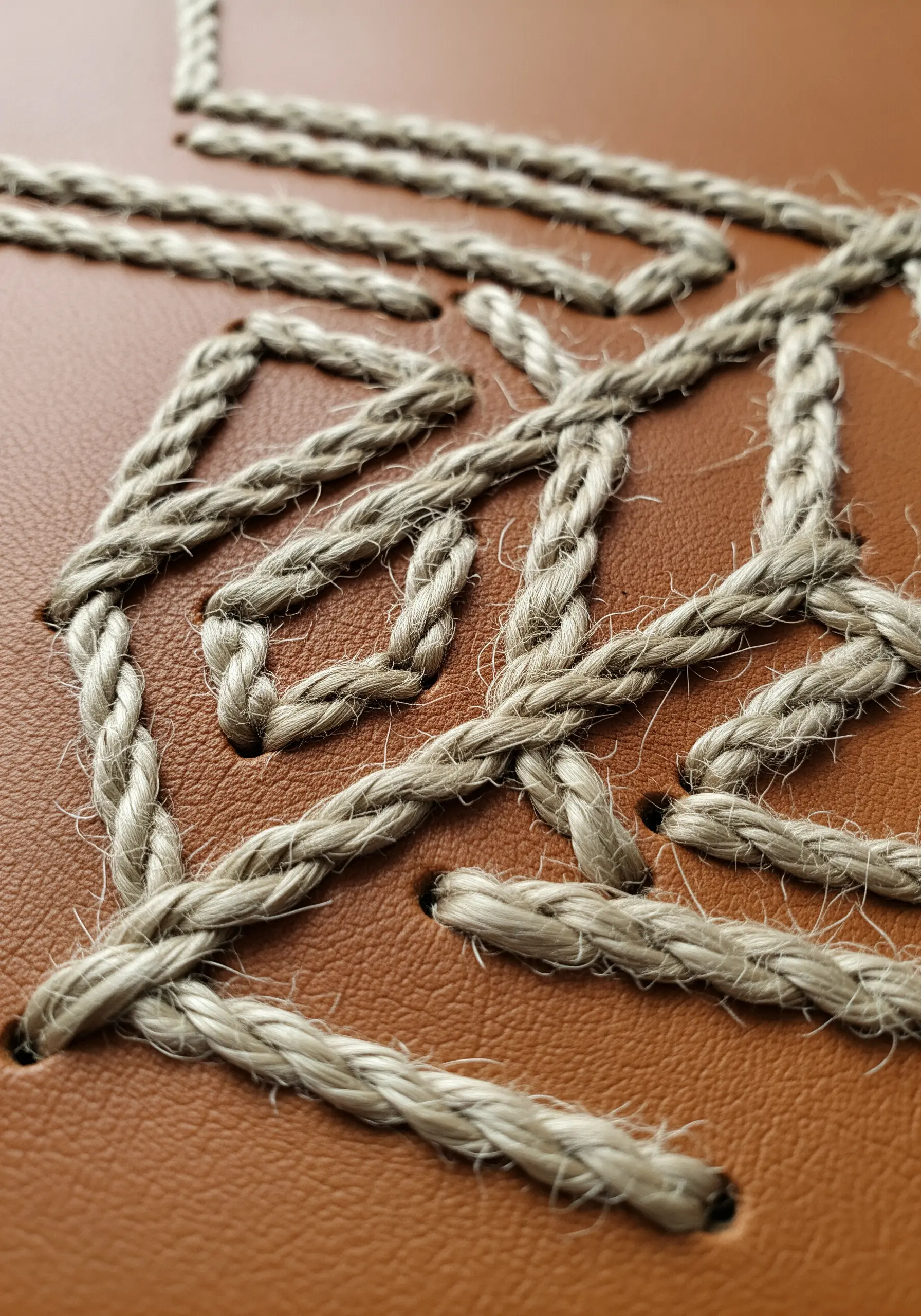A geometric design stitched with thick, rustic twine onto a piece of brown leather.