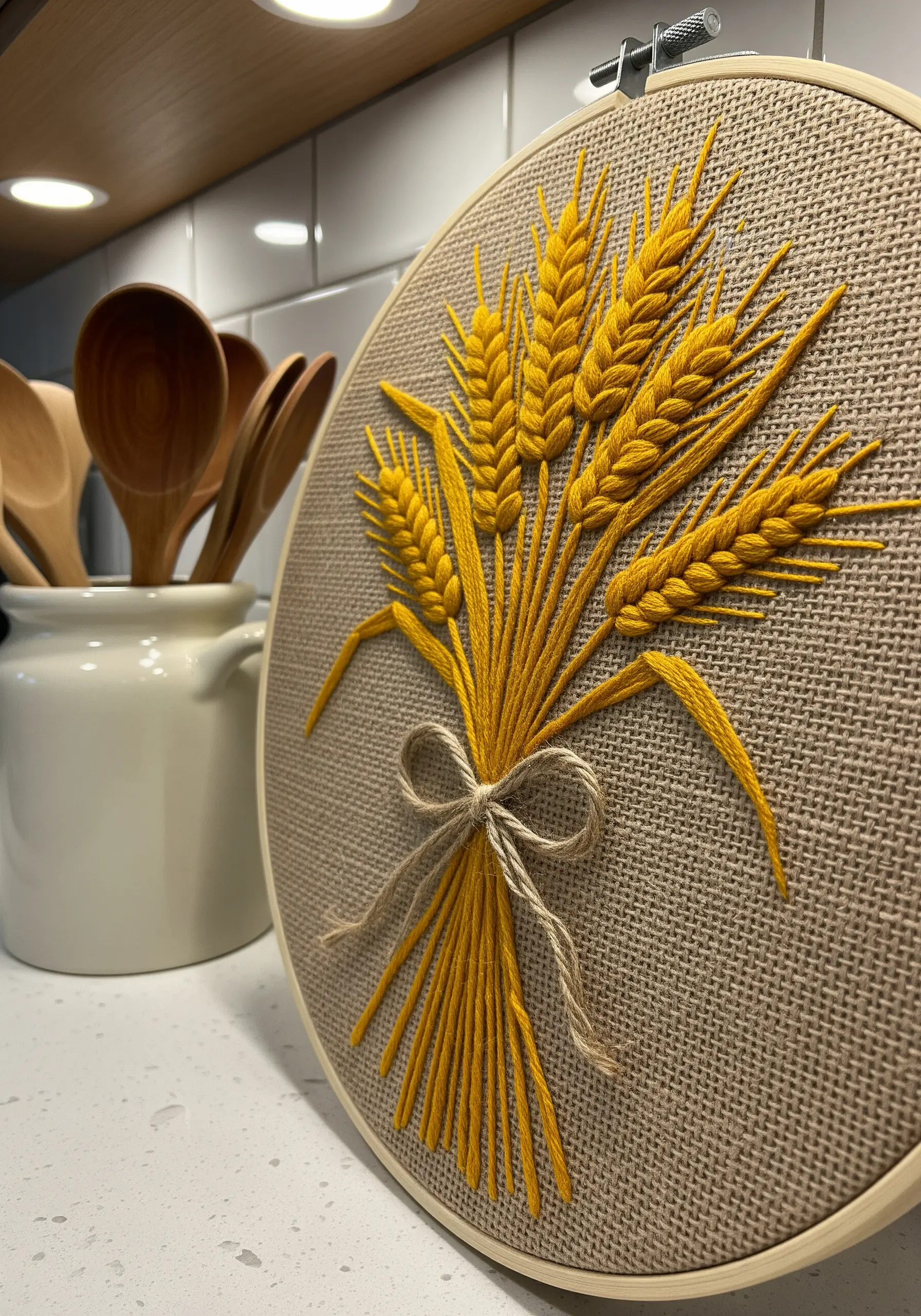 Embroidery of golden wheat stalks on burlap fabric, displayed in a kitchen setting