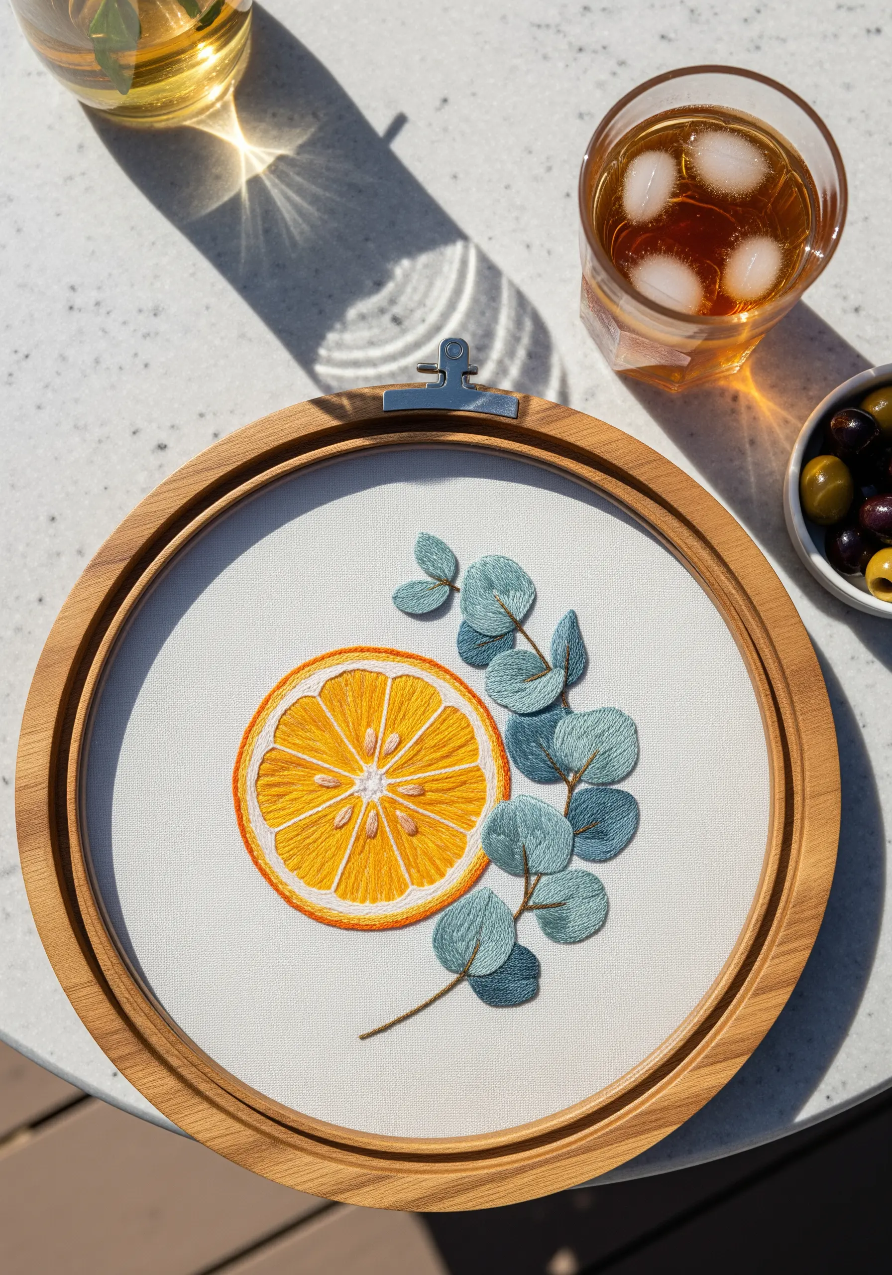 Embroidery hoop art featuring a bright orange slice next to muted green eucalyptus leaves.