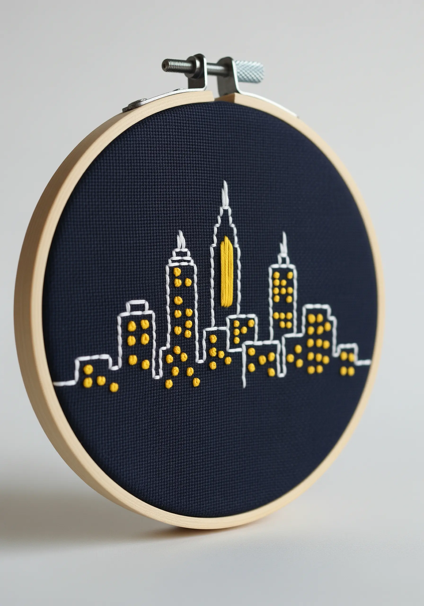 A minimalist embroidery of a city skyline at night on dark blue fabric.