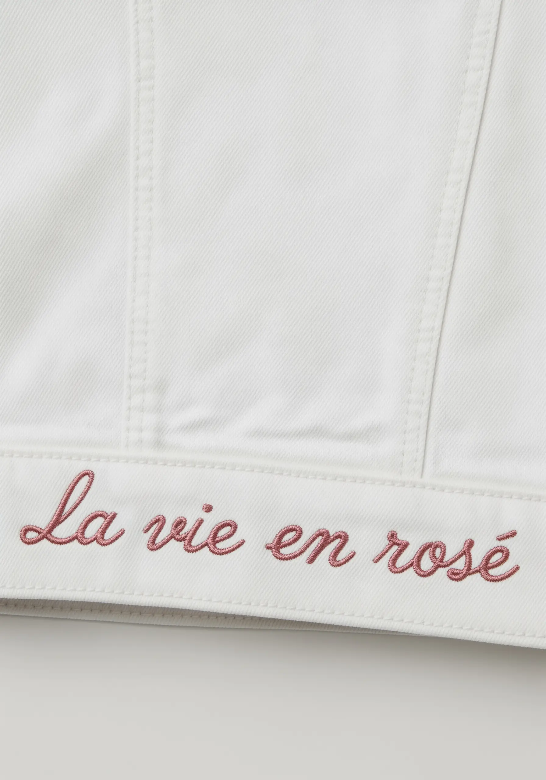 Elegant 'La vie en rosé' script in dusty rose on white denim