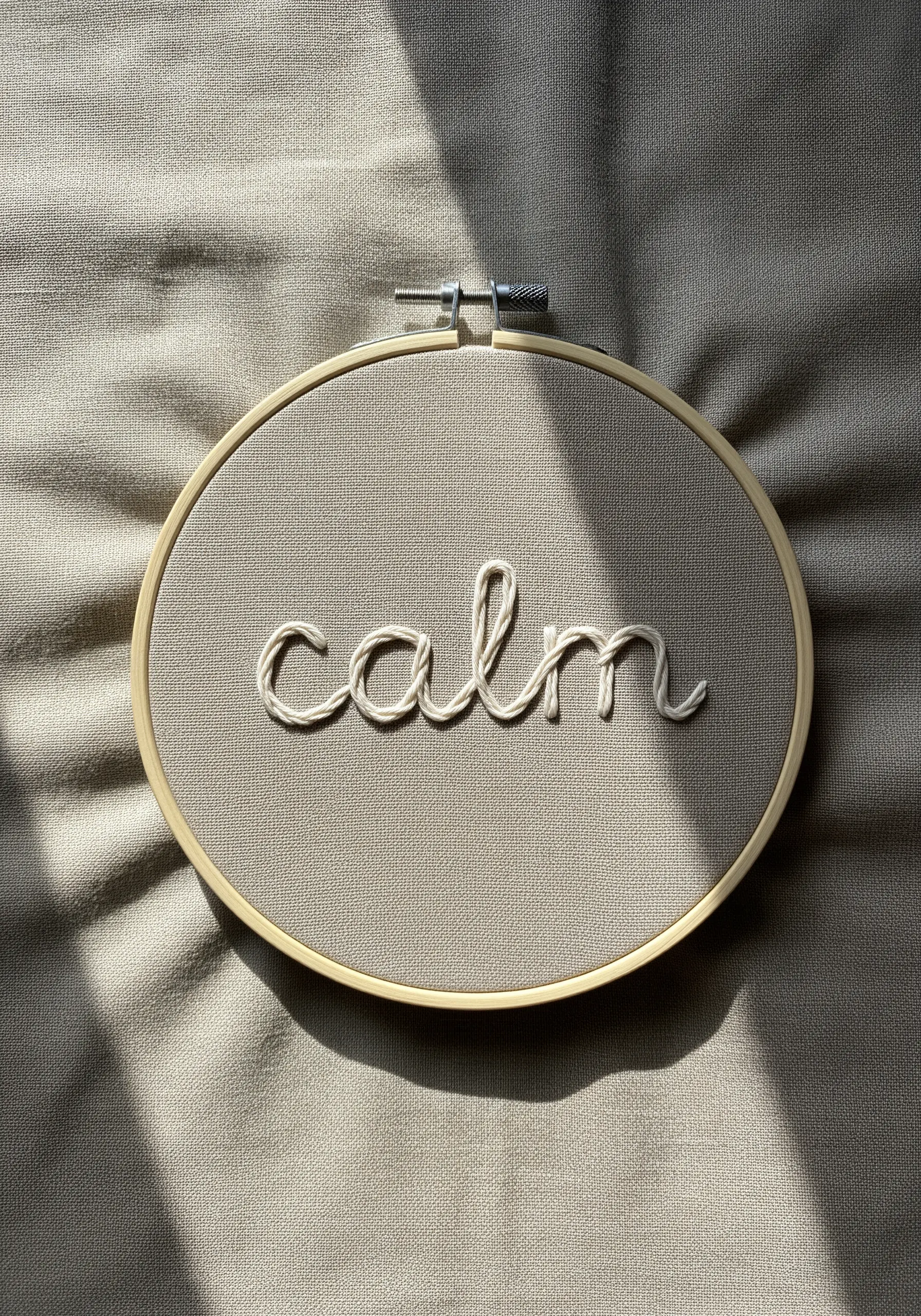 The word 'calm' stitched in flowing cursive with cream thread on taupe fabric.
