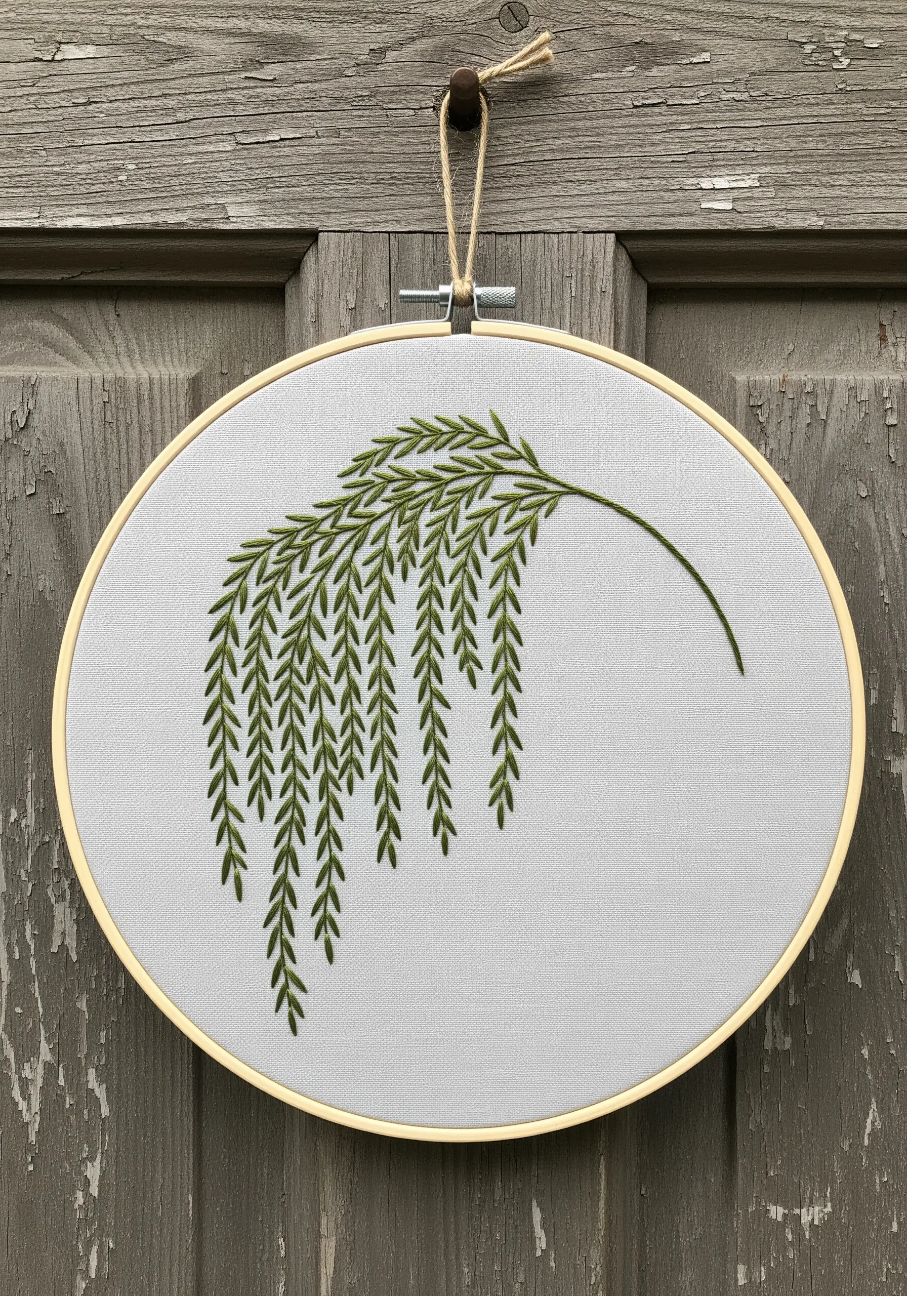 A single weeping willow branch embroidered in green on light gray fabric in an oval hoop.