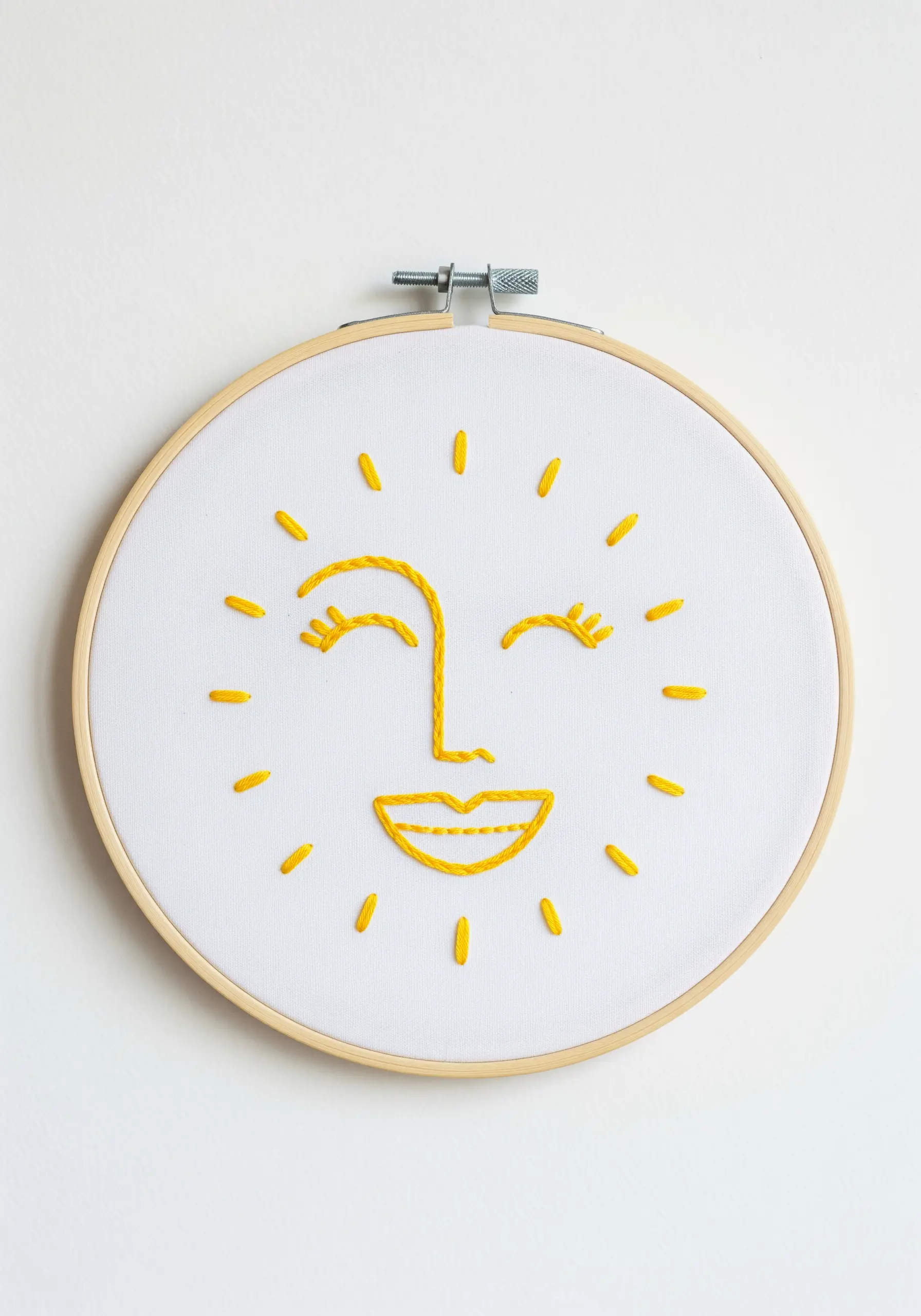 A simple smiling sun face embroidered in yellow thread on white fabric.