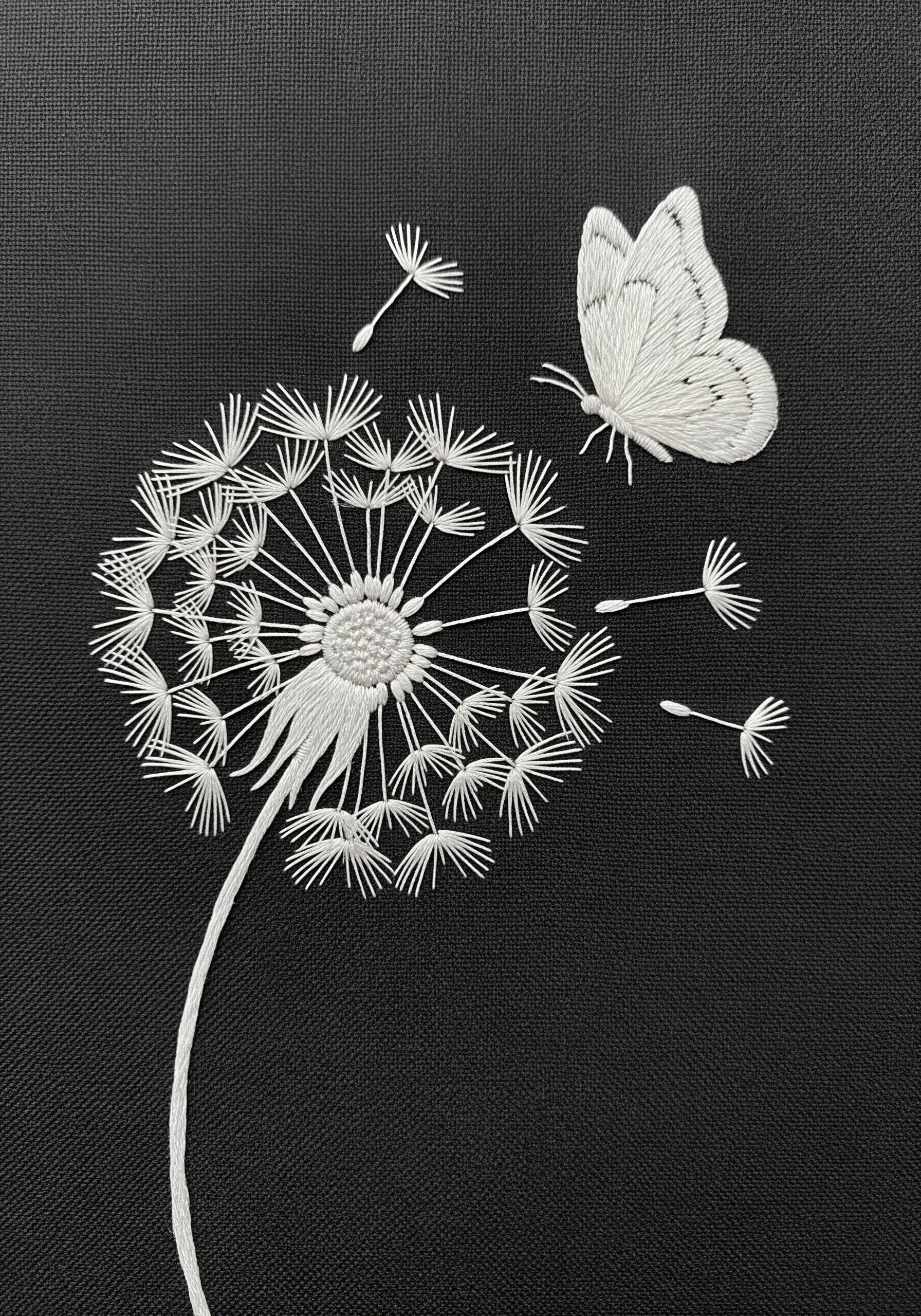 A white-thread embroidery of a dandelion and butterfly on black fabric.