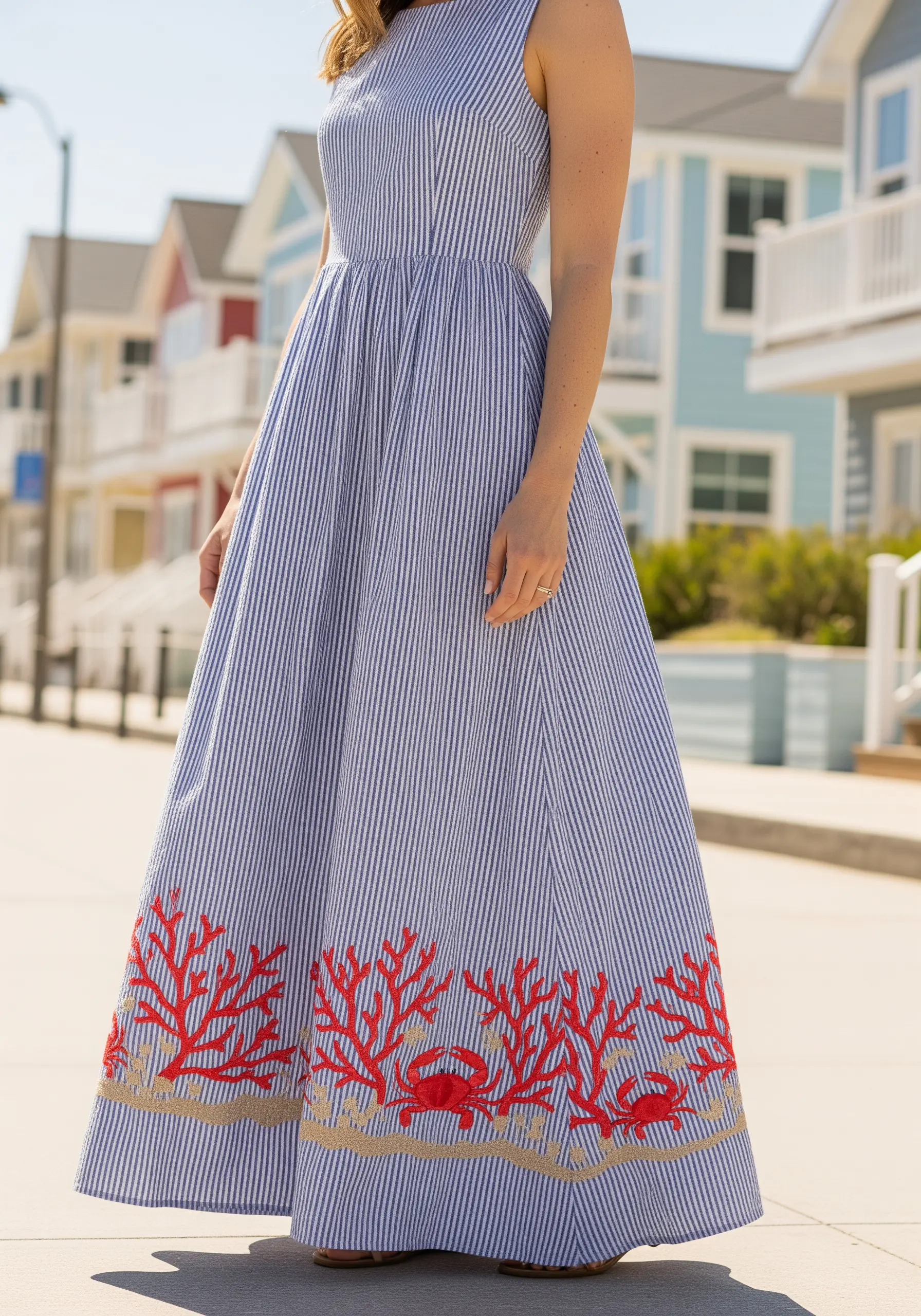 Bright red coral and crab embroidery along the hem of a blue and white striped maxi dress.