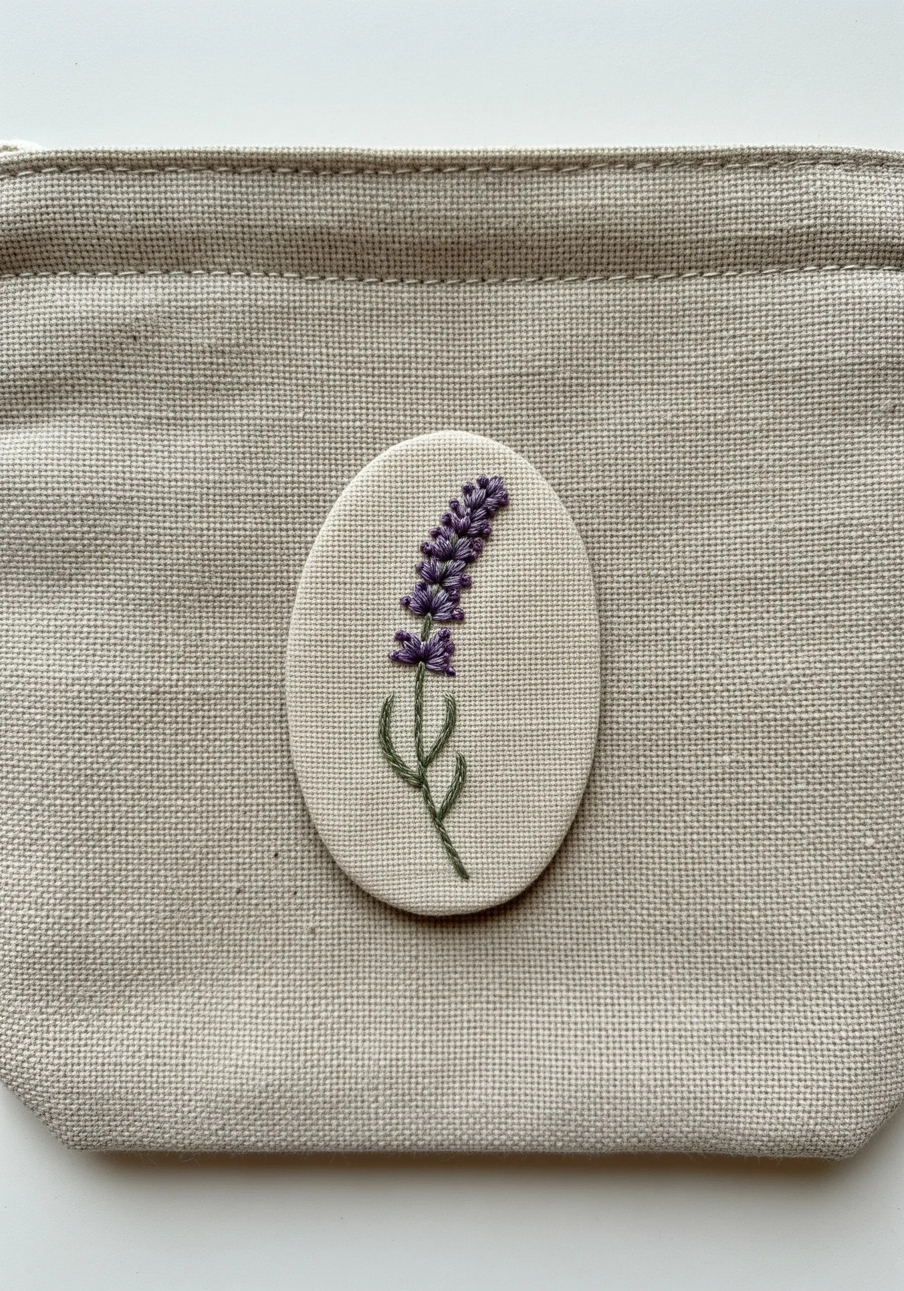 A small oval patch with an embroidered lavender sprig, ready to be sewn onto a canvas pouch.