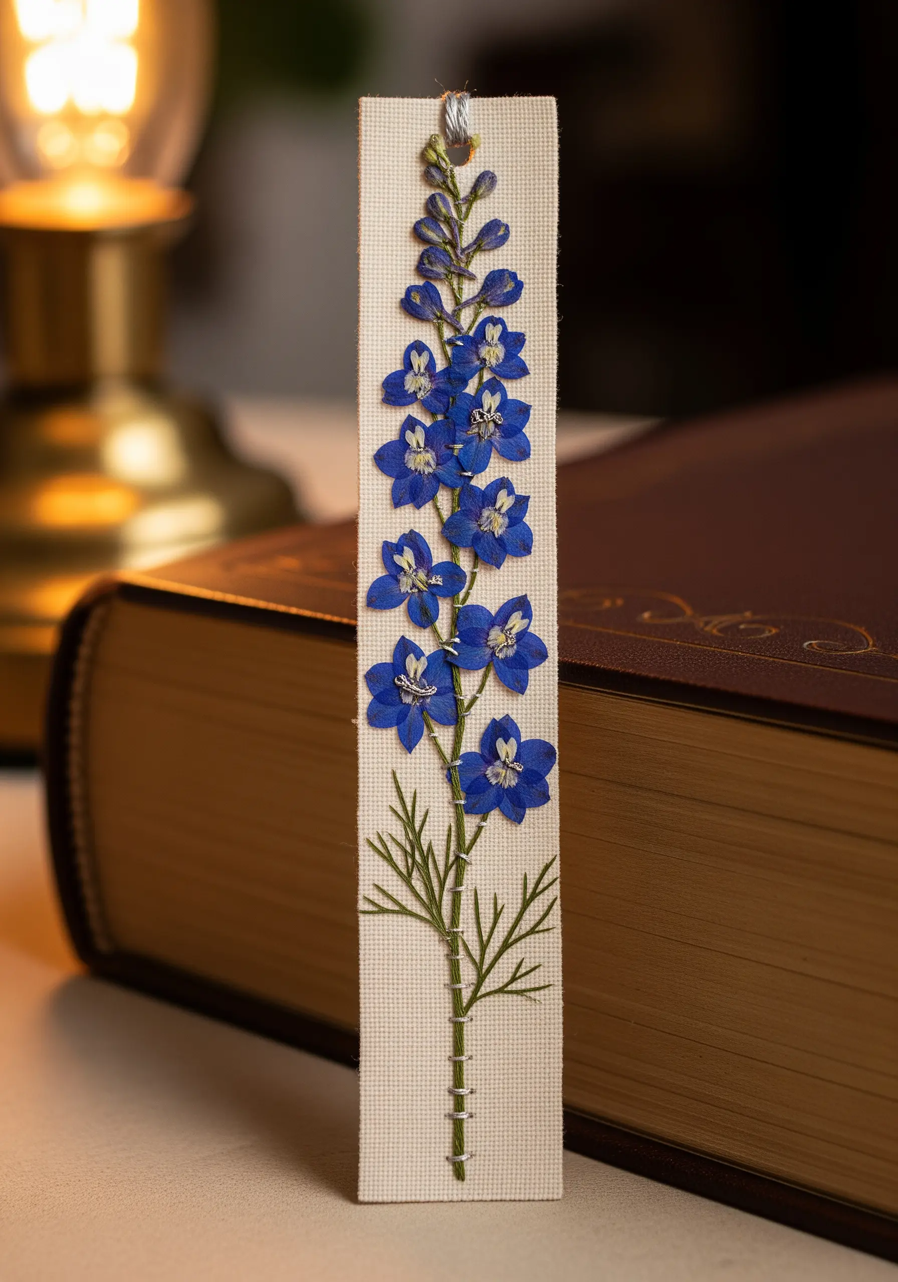 Bookmark featuring a pressed blue delphinium with its lower stem embroidered in green.