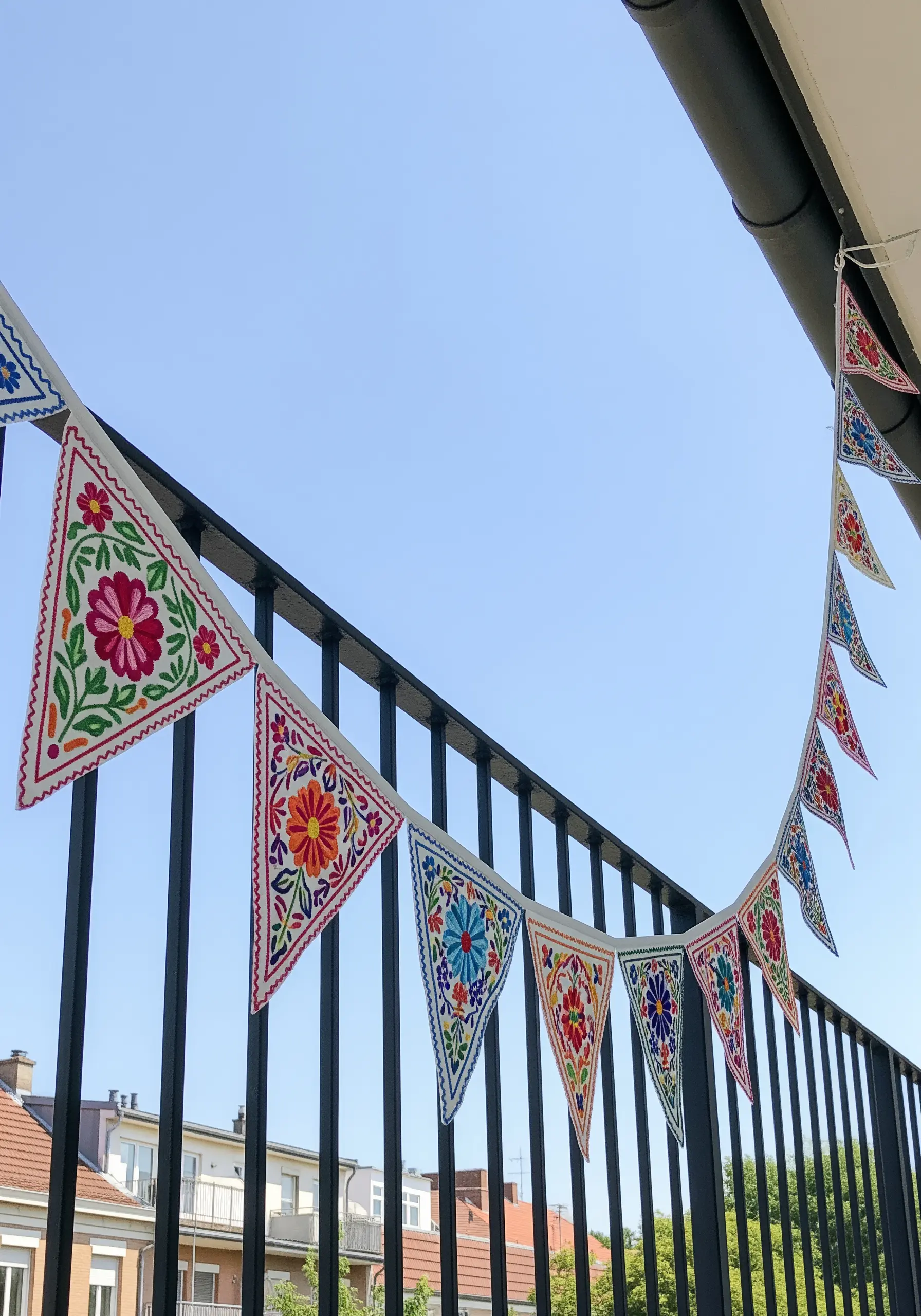 A string of colorful, intricately embroidered floral bunting flags hanging on a balcony.