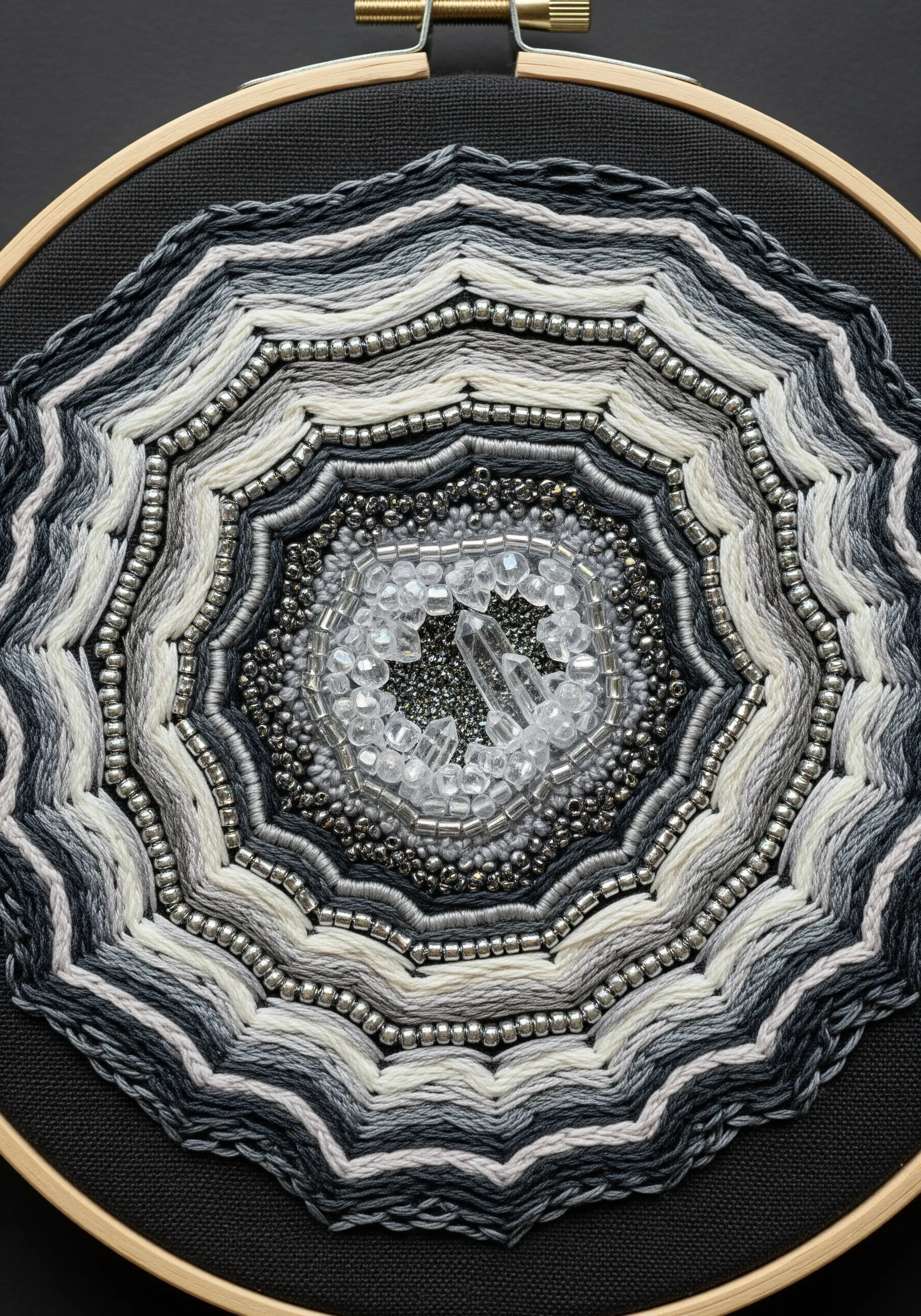 Close-up of a beaded and embroidered geode with a central crystal on black fabric.