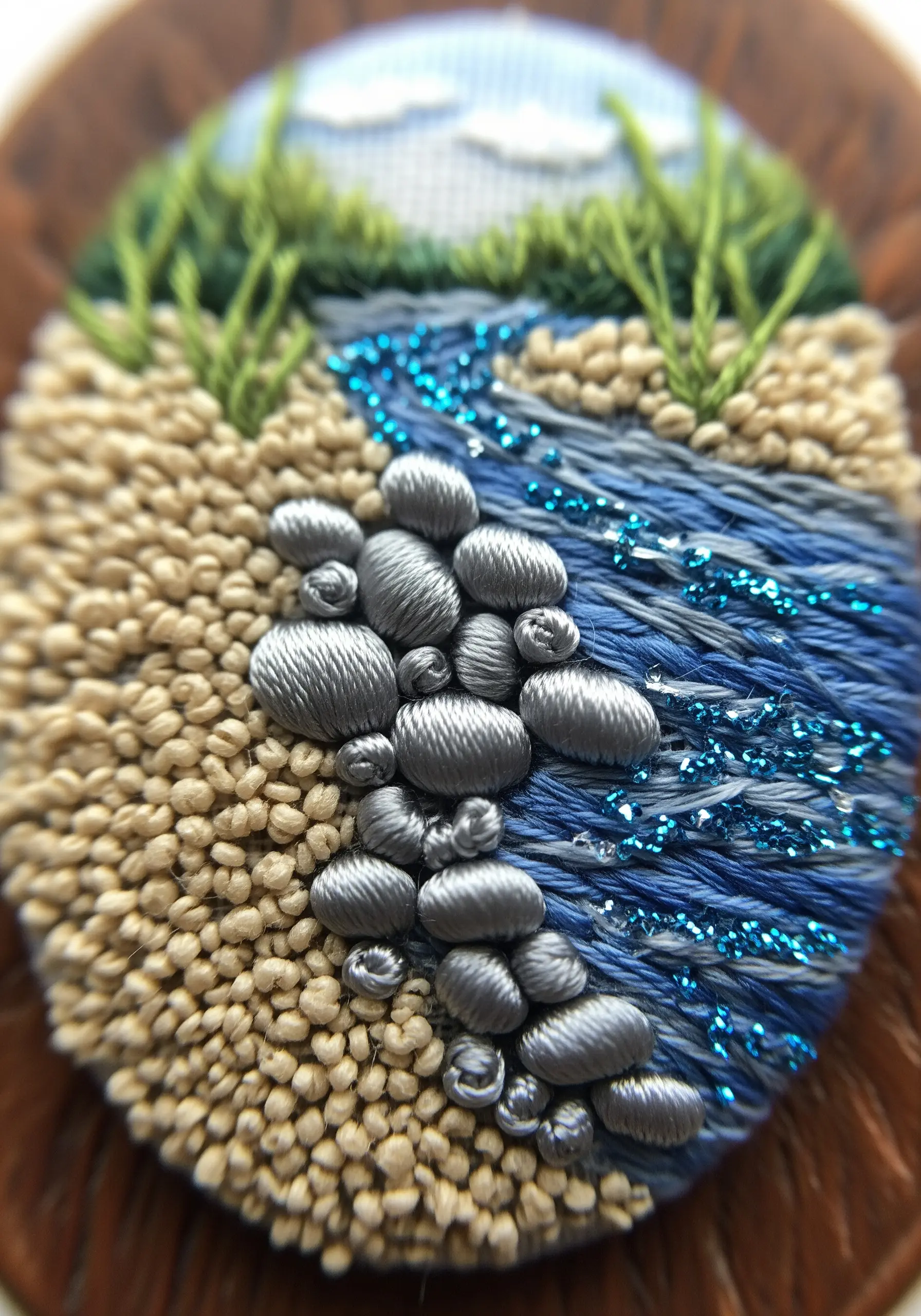 Close-up of a miniature embroidered river scene with satin stitch stones and French knots.