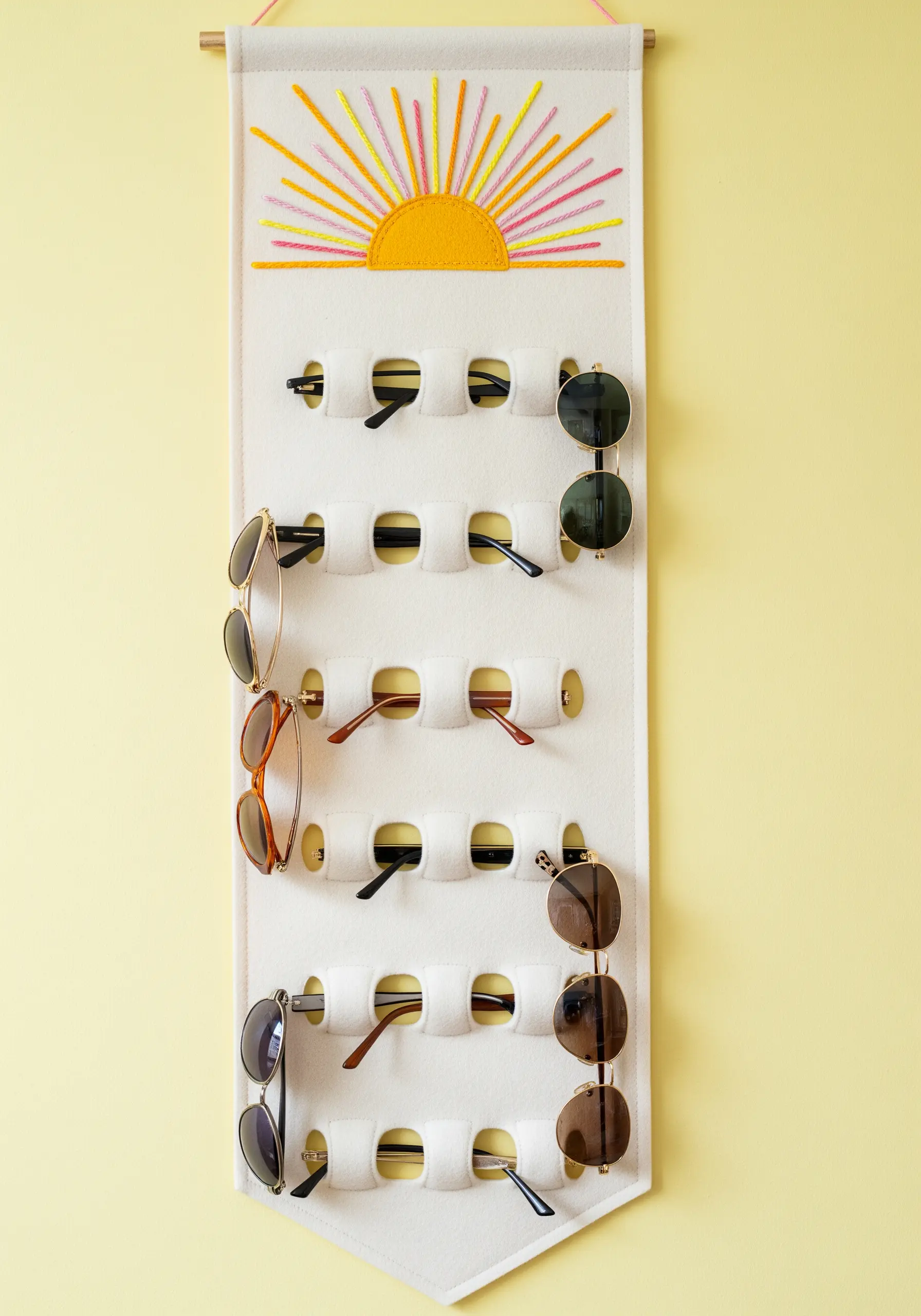 A felt wall hanging with an embroidered sunburst at the top, used to organize sunglasses.