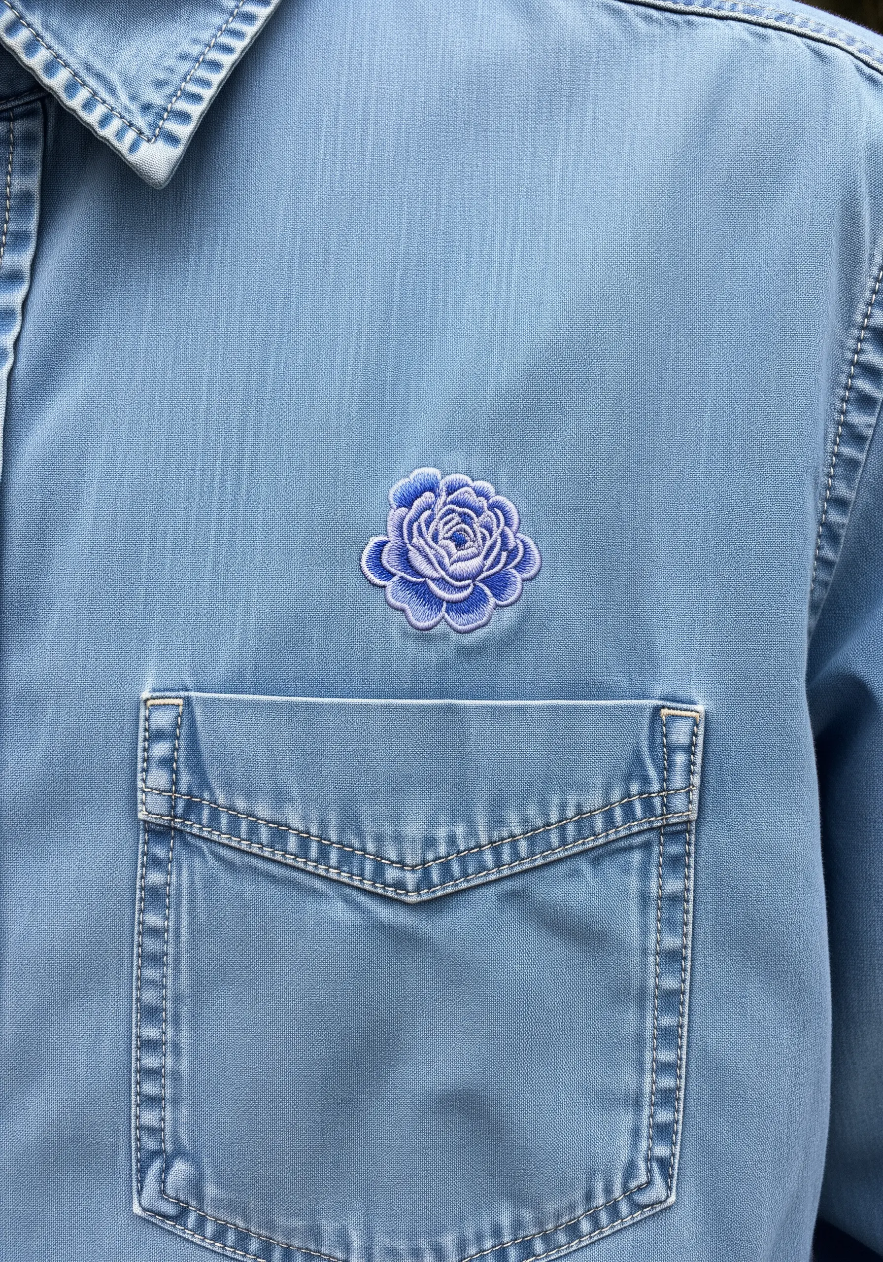 A small blue peony patch stitched above the pocket of a chambray shirt.